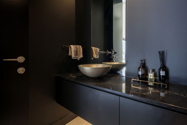 Moody contemporary bathroom vanity with matte black walls and cabinetry, a dark marble-look benchtop, brushed metal vessel basin and tapware, a large mirror, and neatly arranged toiletries and towels.