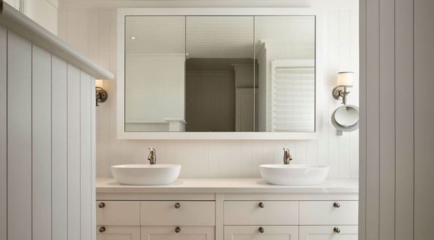 Bright, symmetrical bathroom vanity with two white vessel basins, brushed metal taps, a wide frameless mirror, white vertical wall panelling, and a pale painted timber vanity with drawers. Traditional detailing is paired with clean, restrained styling.