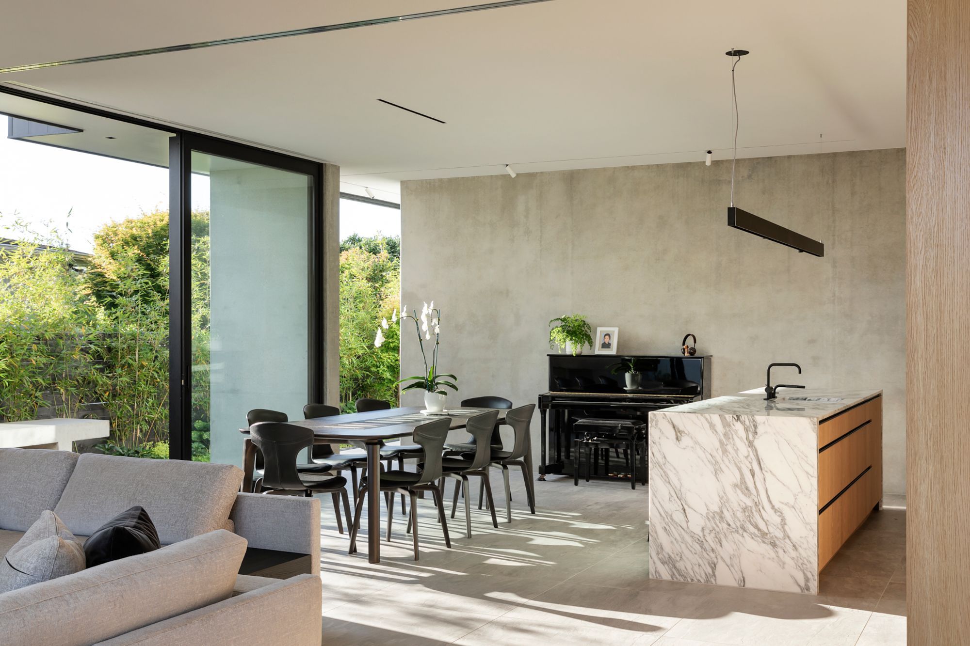 A black piano takes centrestage against a polished concrete wall while the beautiful veining in the marble kitchen island competes with the bamboo shadows on the floor.