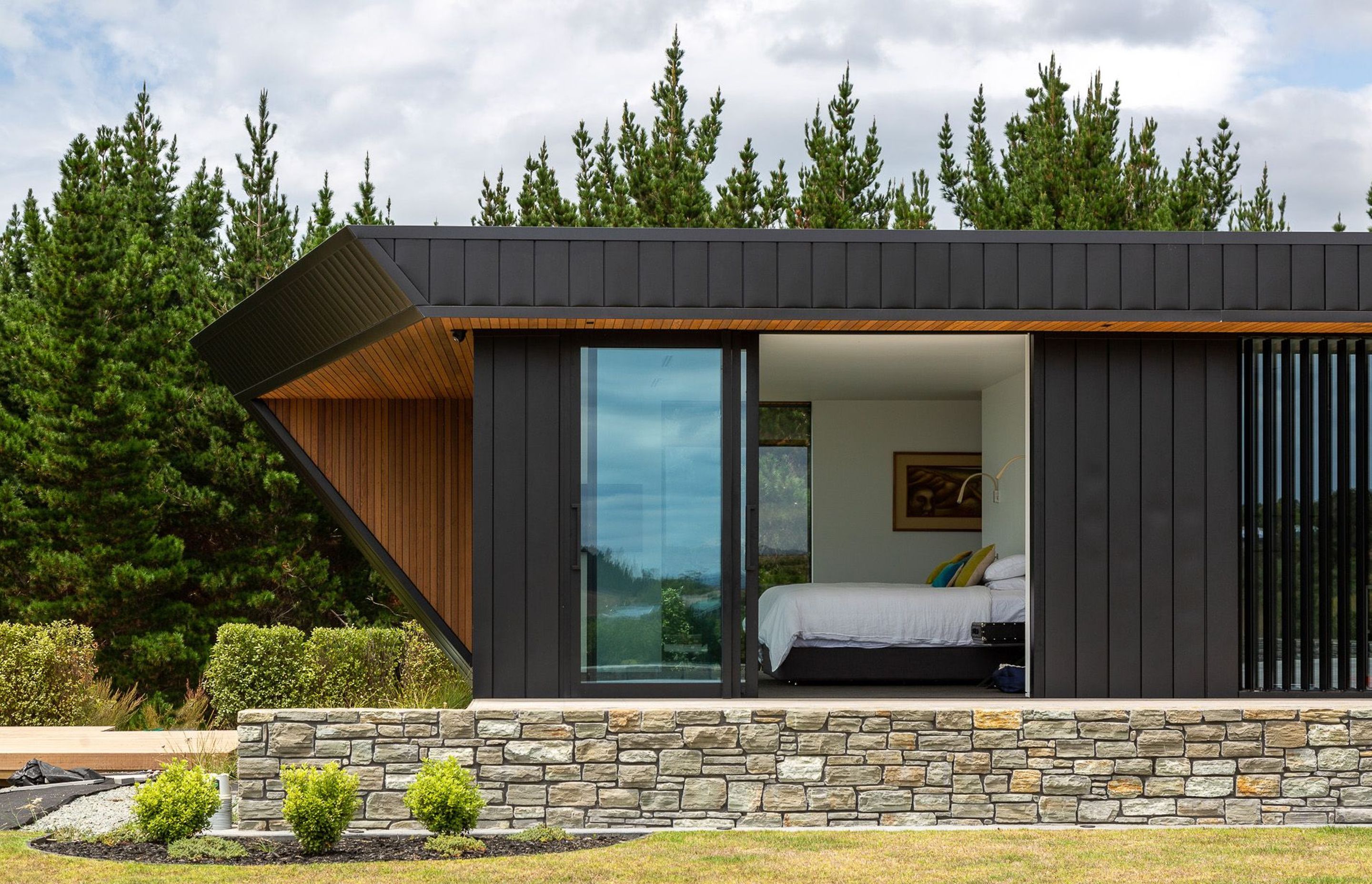 The cedar-clad overhangs create dramatic angles, a sense of movement and a visual focal point in their departure from the black vertical aluminium cladding that graces the rest of the exterior.