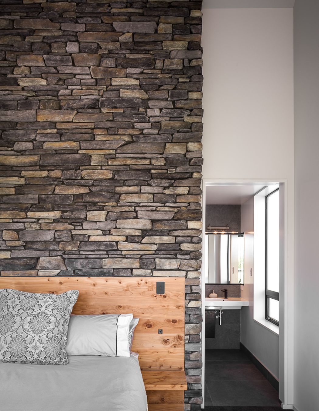 A stone feature wall with built-in timber headboard makes a bold statement in this master bedroom suite.