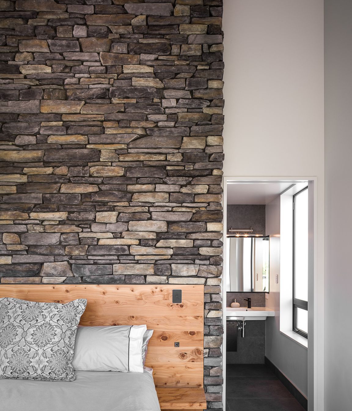 A stone feature wall with built-in timber headboard makes a bold statement in this master bedroom suite.