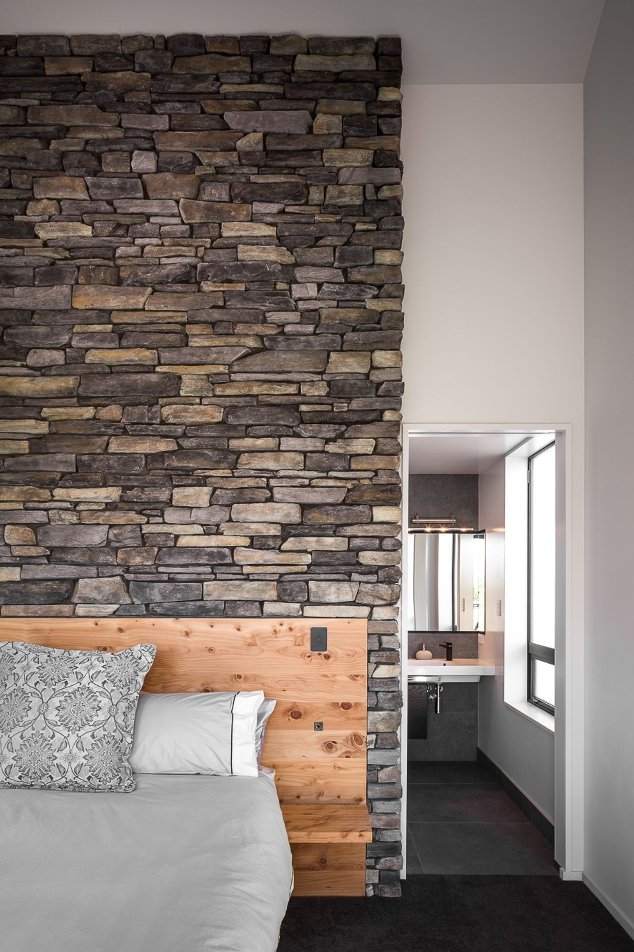A stone feature wall with built-in timber headboard makes a bold statement in this master bedroom suite.