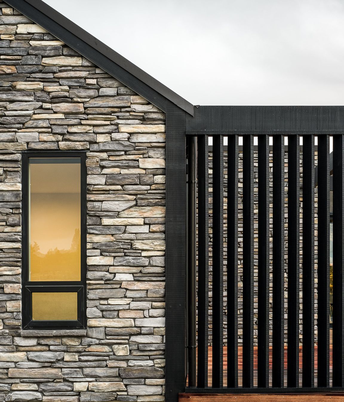 Dark stained vertical cedar frames the main body of the house with gable end accents and feature walls of Schist stone combining to create a solid and defined house.