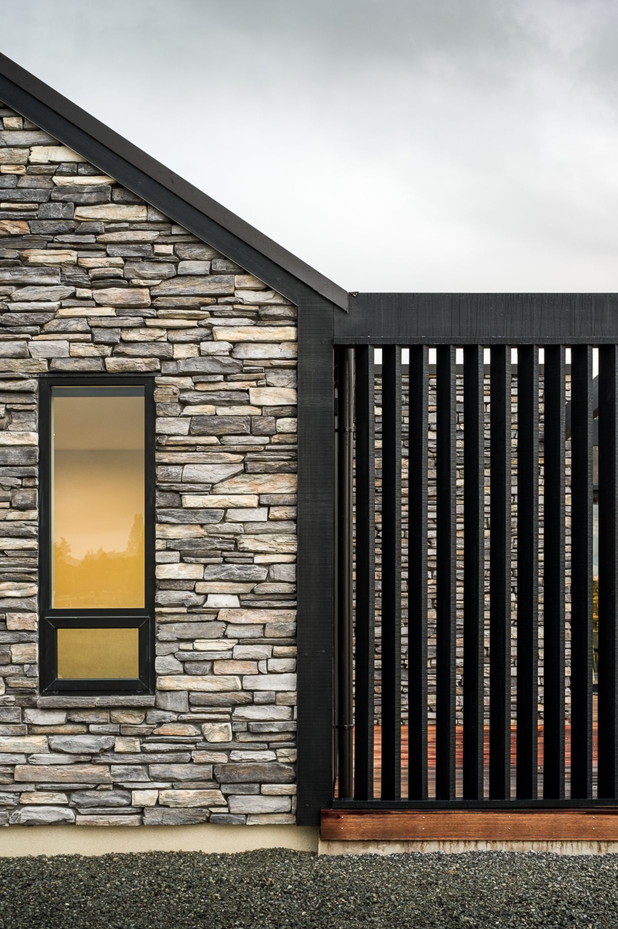 Dark stained vertical cedar frames the main body of the house with gable end accents and feature walls of Schist stone combining to create a solid and defined house.