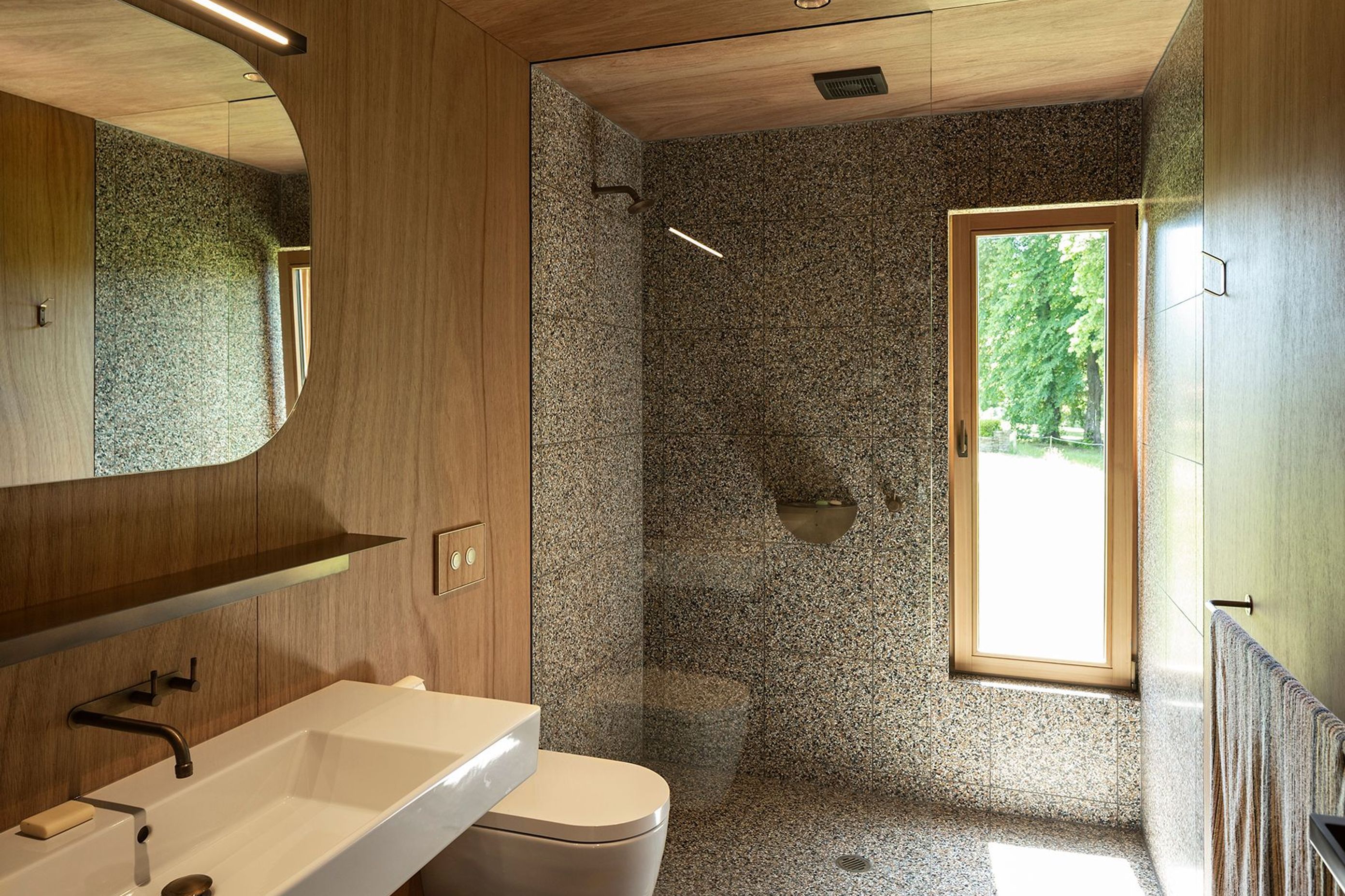 Timber cabinetry continues into the bathroom space with its distinctive speckled tiling and bronze tapware.
