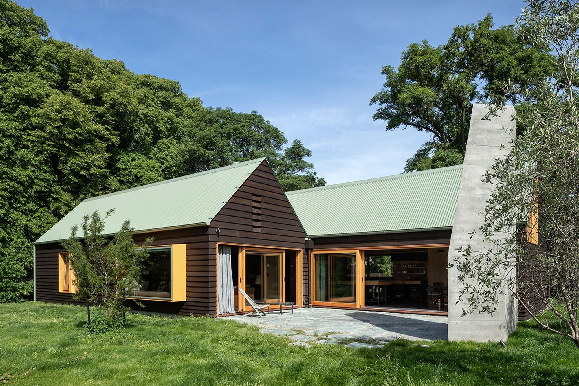 Chocolate-brown cedar weatherboards, sage-green metal roofing and mustard-yellow windows add familiarity to this cosy family dwelling in Wanaka.