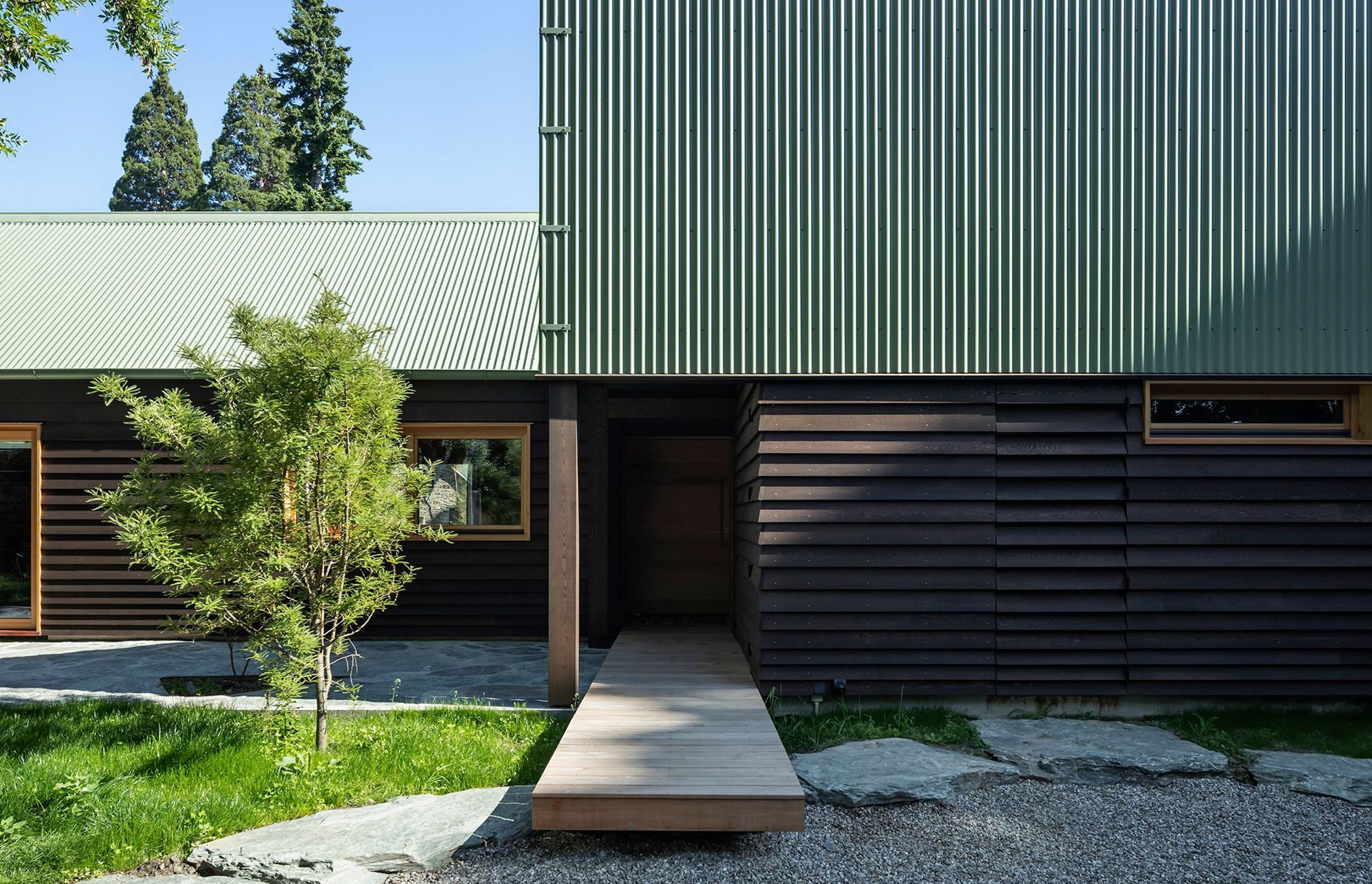 At the edge of the chisel form, an entry boardwalk floats over large stones before disappearing under the chiselled roof to form a semi-enclosed walkway.