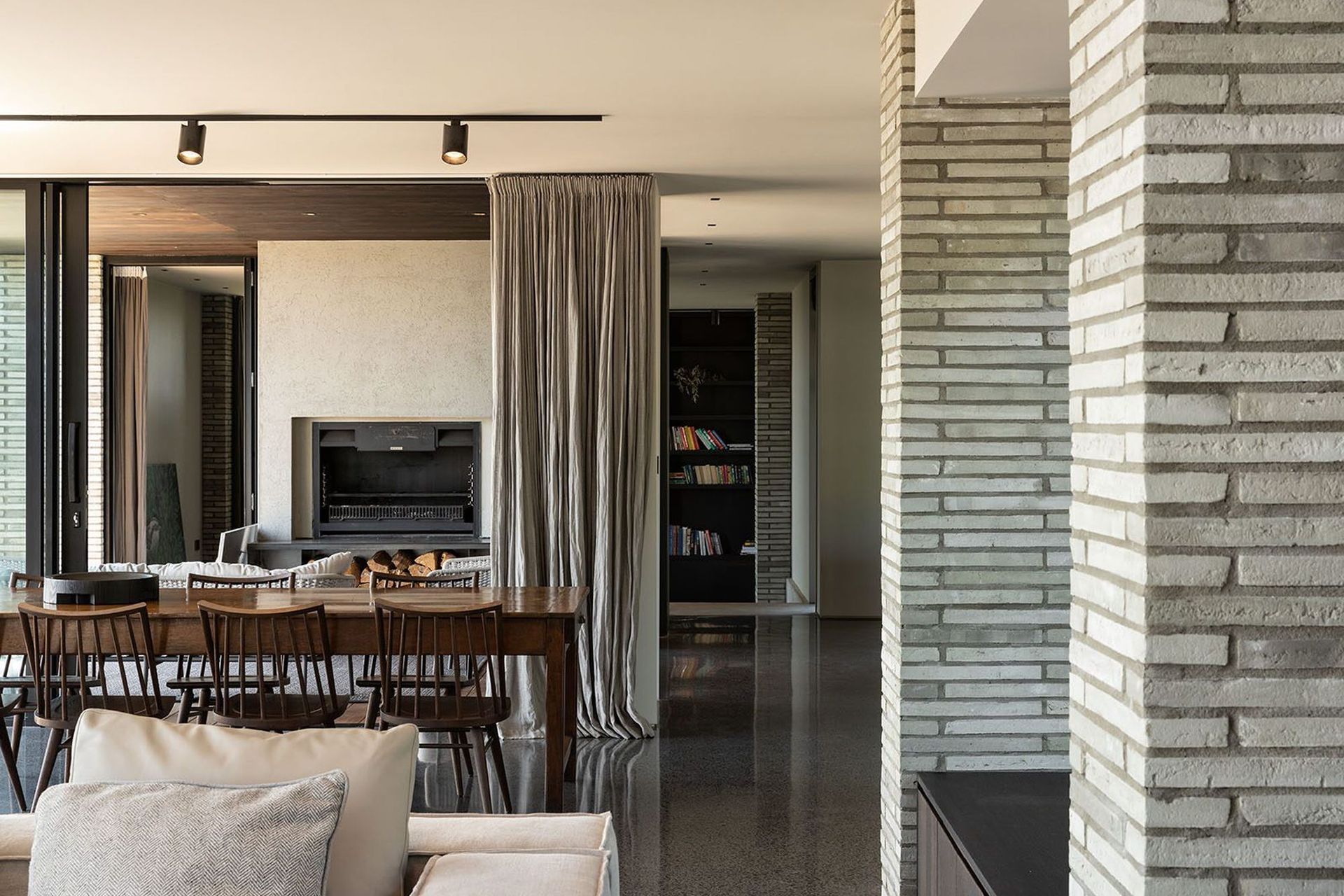 Beyond the kitchen to the east, an enclosed deck conceives an ambiguity between inside and out. Here, an open wood fire takes pride of place, while the charred timber of the exterior wraps around to form the ceiling of this undefined space.