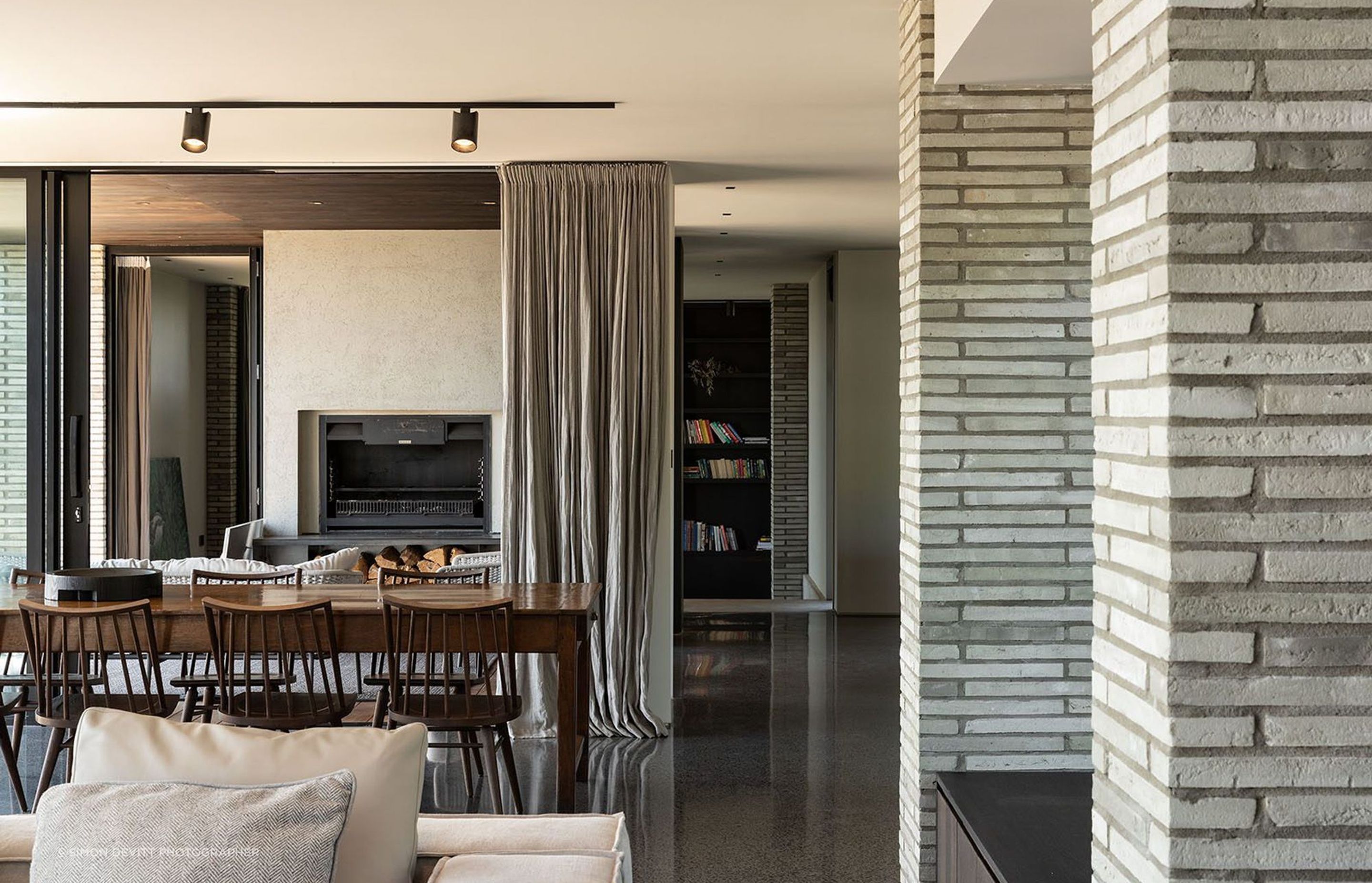 Beyond the kitchen to the east, an enclosed deck conceives an ambiguity between inside and out. Here, an open wood fire takes pride of place, while the charred timber of the exterior wraps around to form the ceiling of this undefined space.