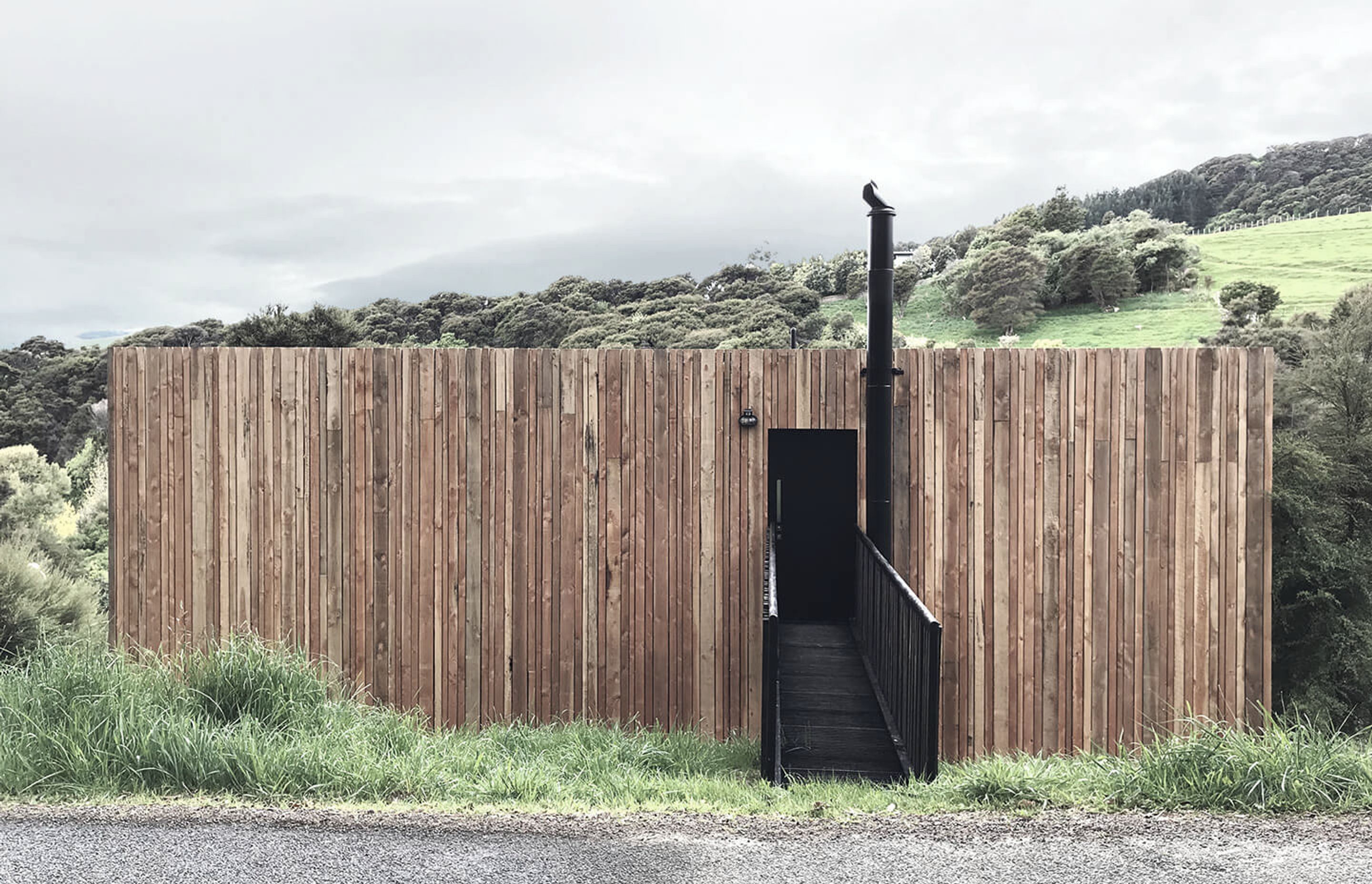 The black entrance forms a void within the timber-clad envelope which wraps around the home and sympathetically sits within the manuka-clad and rural landscape.