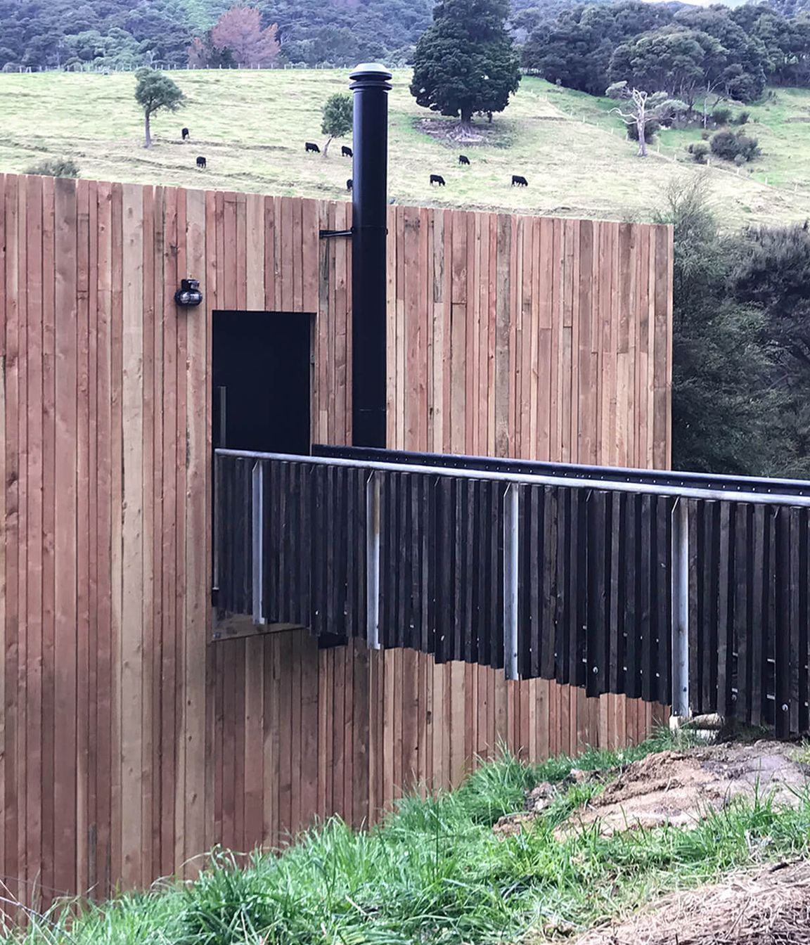 A close-up view shows the vertical lines of the Doublas fir weatherproof rainscreen against the timber and black-steel structure of the bridged entranceway.