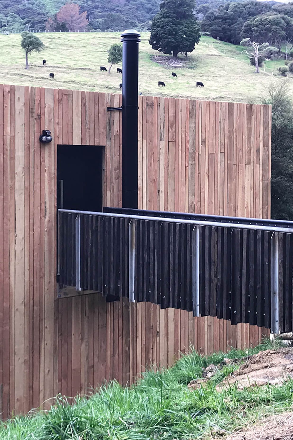 A close-up view shows the vertical lines of the Doublas fir weatherproof rainscreen against the timber and black-steel structure of the bridged entranceway.