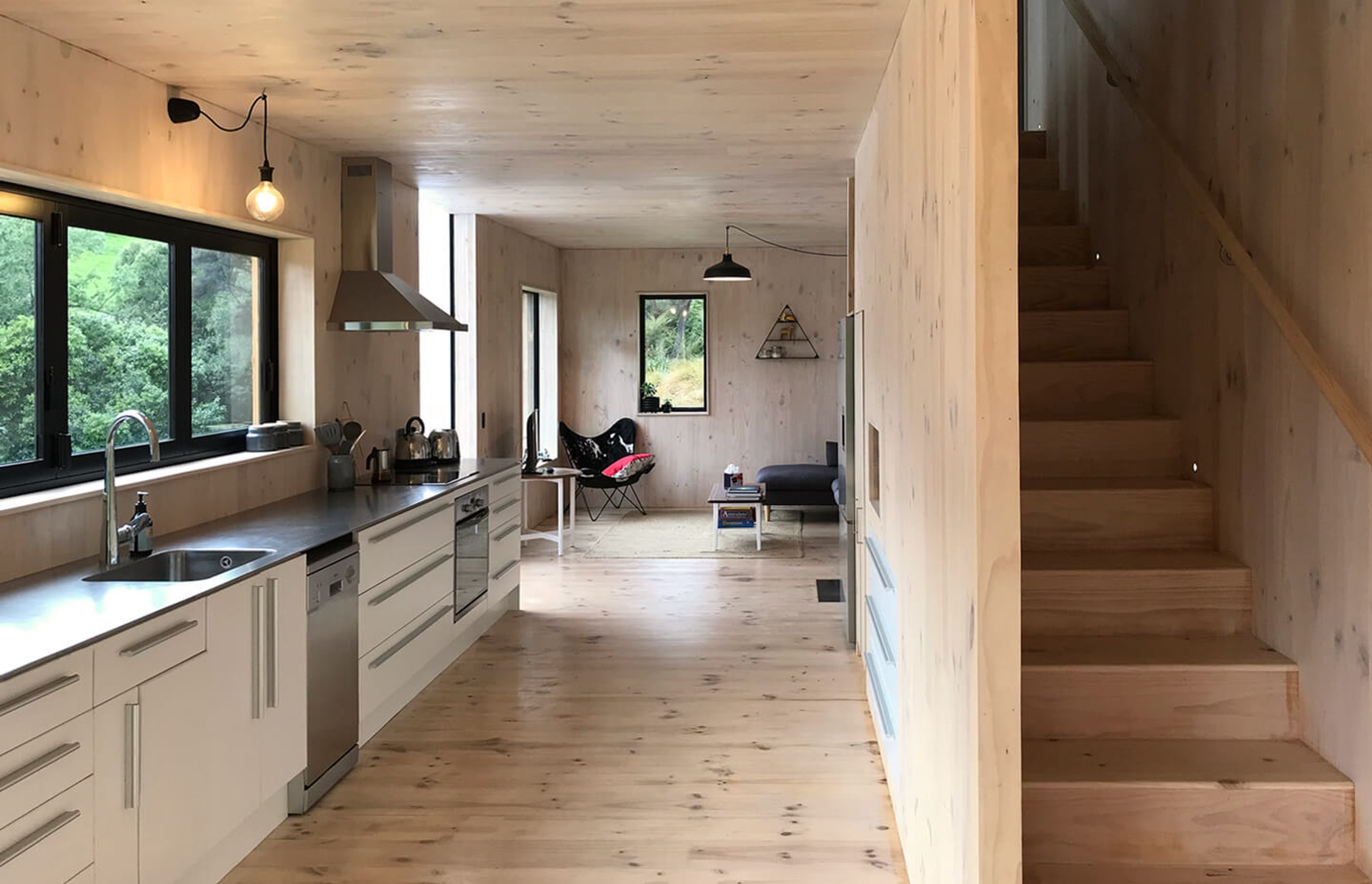 The living space at the far end leads tthrough to the repurposed kitchen with a stainless steel benchtop that matches the practical nature of the home. The timber  staircase has built-in storage.