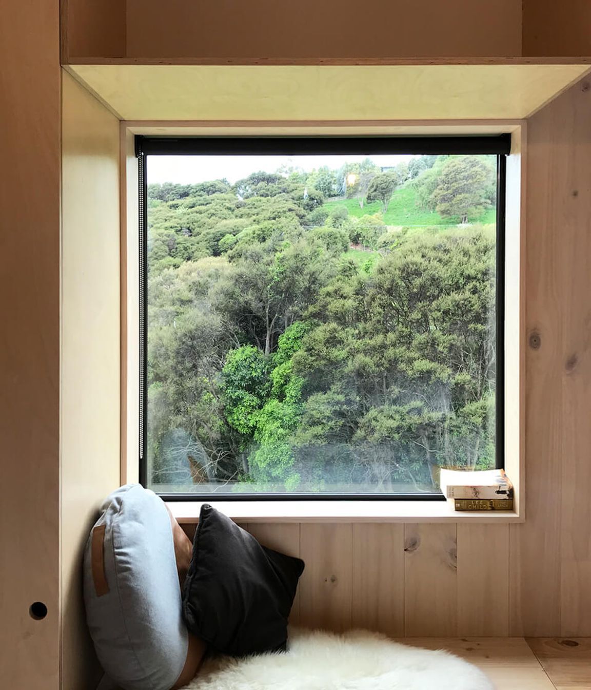 A built-in window seat looks out to a manuka bush-clad hillside and grazing farm animals.