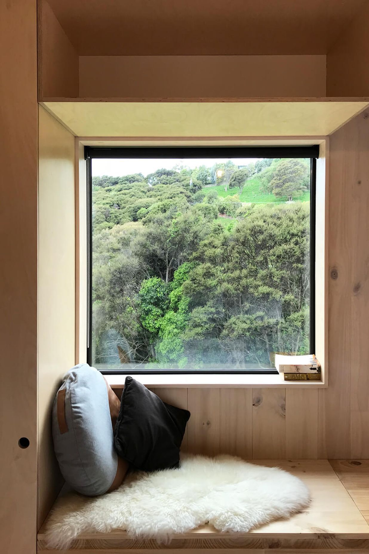 A built-in window seat looks out to a manuka bush-clad hillside and grazing farm animals.