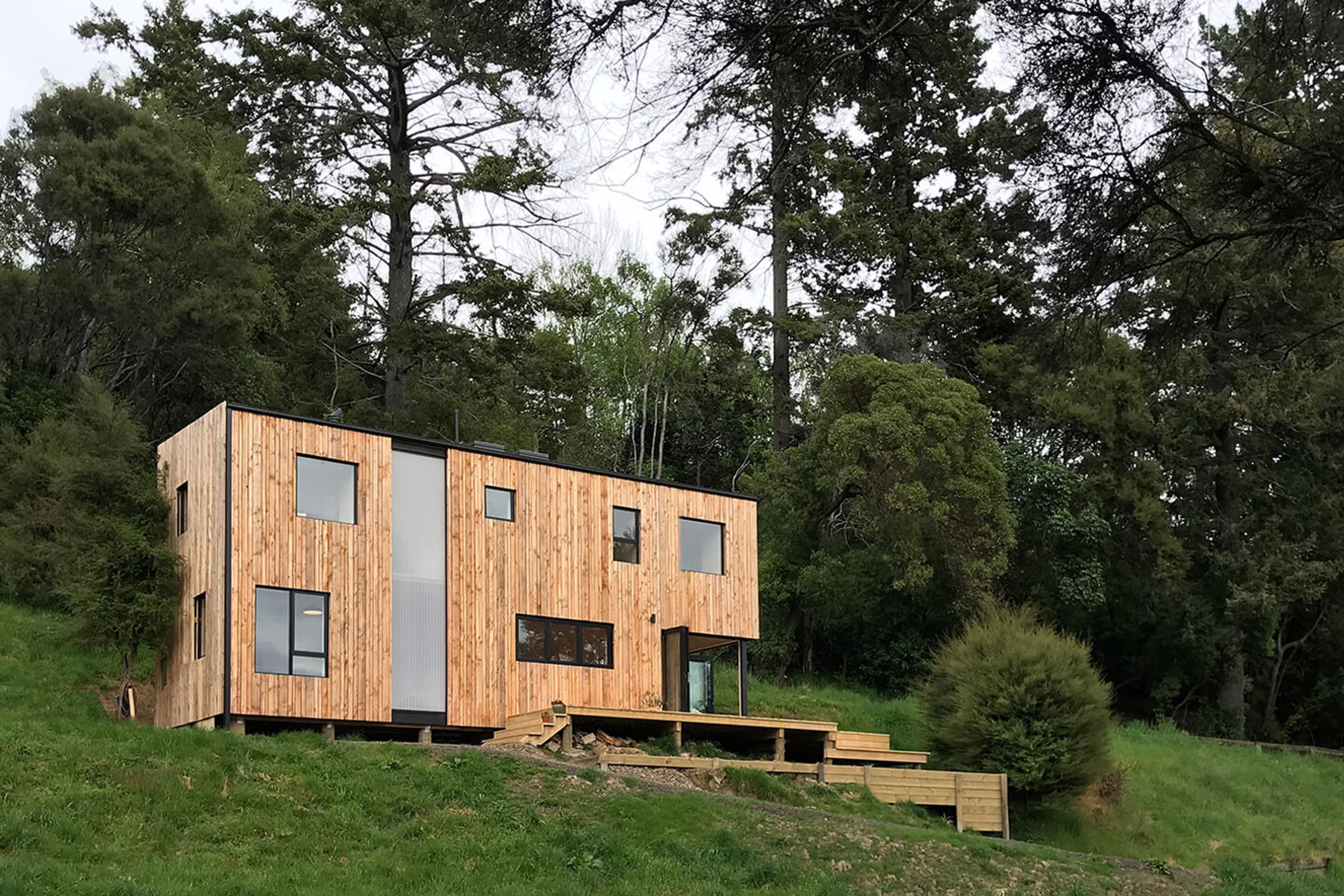 The Akaroa bach faces north over the valley and is clad in timber with a polycarbonate insert that lights up like a beacon at night and draws natural light into the interior by day.