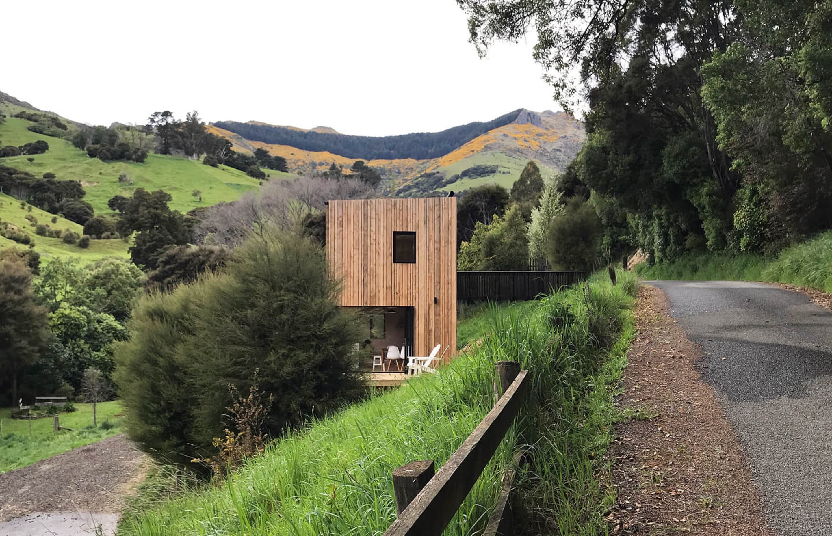 Akaroa Bach from the road showing the verticality of the home nestled into the steep slope with a bridged entranceway from the roadside.