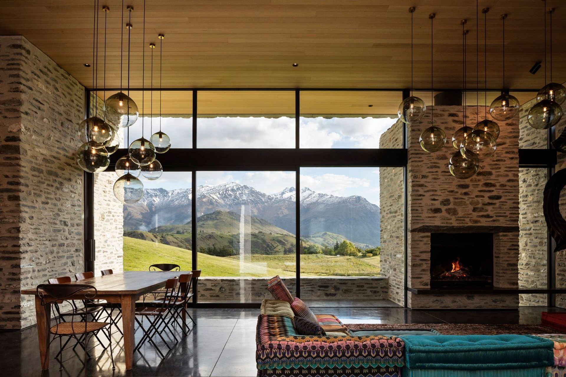 In the living space, glazing rises up from the floor and over the top of a stone chimney, washing sunlight over the interior to accentuating the rich texture of the schist.