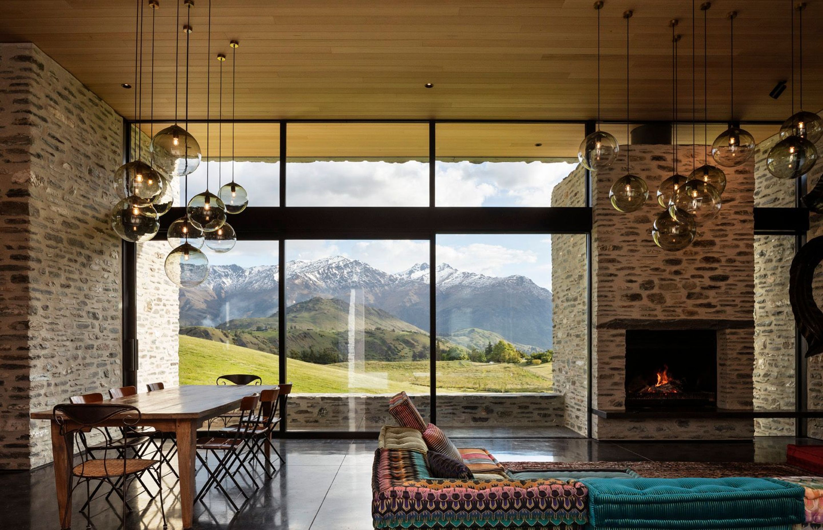 In the living space, glazing rises up from the floor and over the top of a stone chimney, washing sunlight over the interior to accentuating the rich texture of the schist.