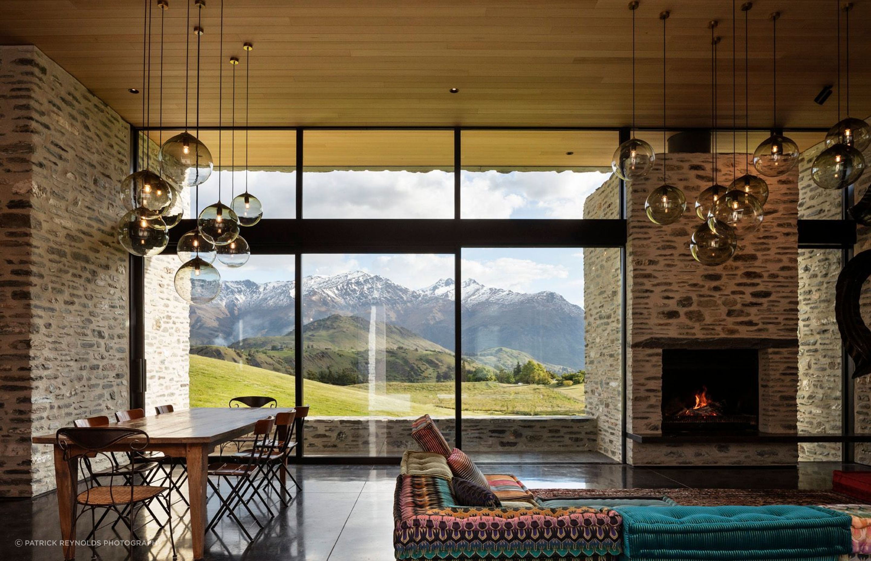 In the living space, glazing rises up from the floor and over the top of a stone chimney, washing sunlight over the interior to accentuating the rich texture of the schist.