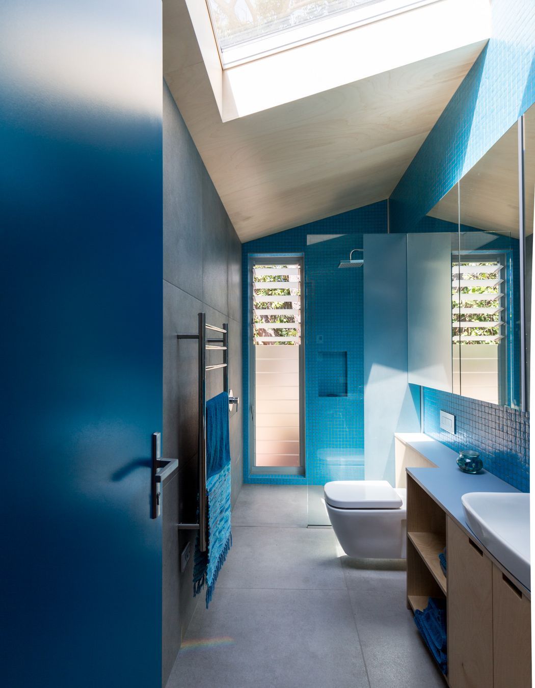 A large skylight admits natural light into the azure-coloured bathroom.