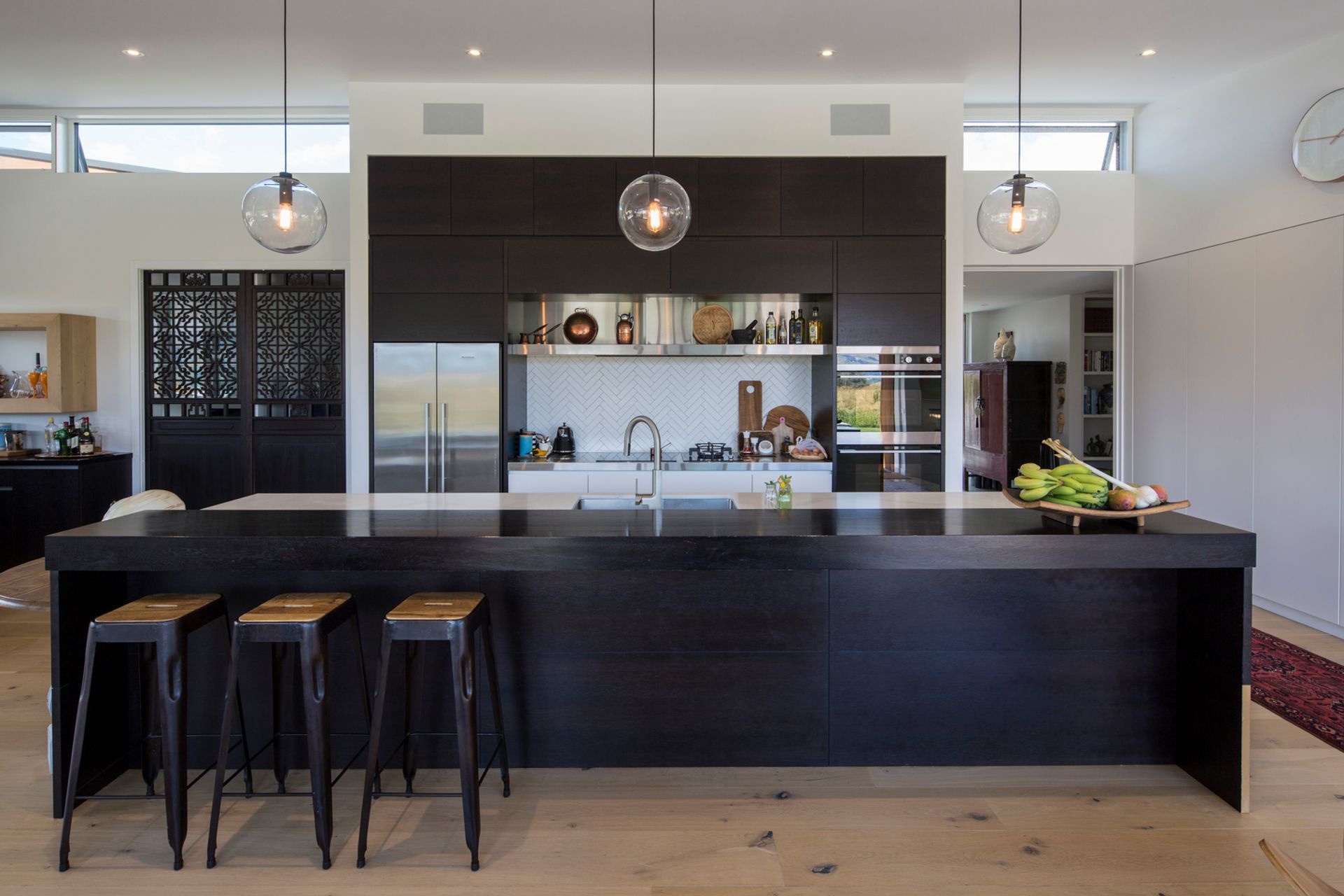 Set up to entertain, the galley-style kitchen features a large island bench with raised seating area. The dark stained timber cabinetry contrasts the neutral palette, while statement doors add a touch of texture.