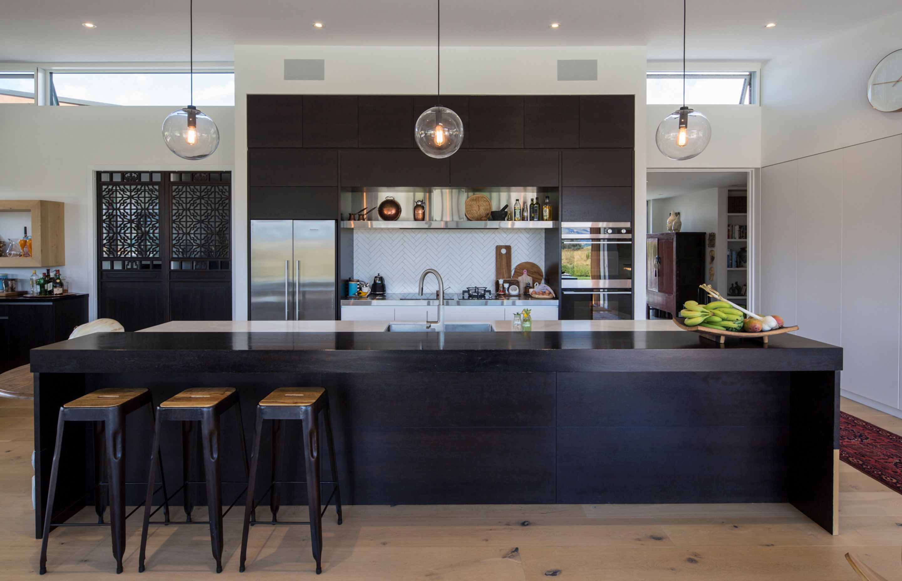 Set up to entertain, the galley-style kitchen features a large island bench with raised seating area. The dark stained timber cabinetry contrasts the neutral palette, while statement doors add a touch of texture.