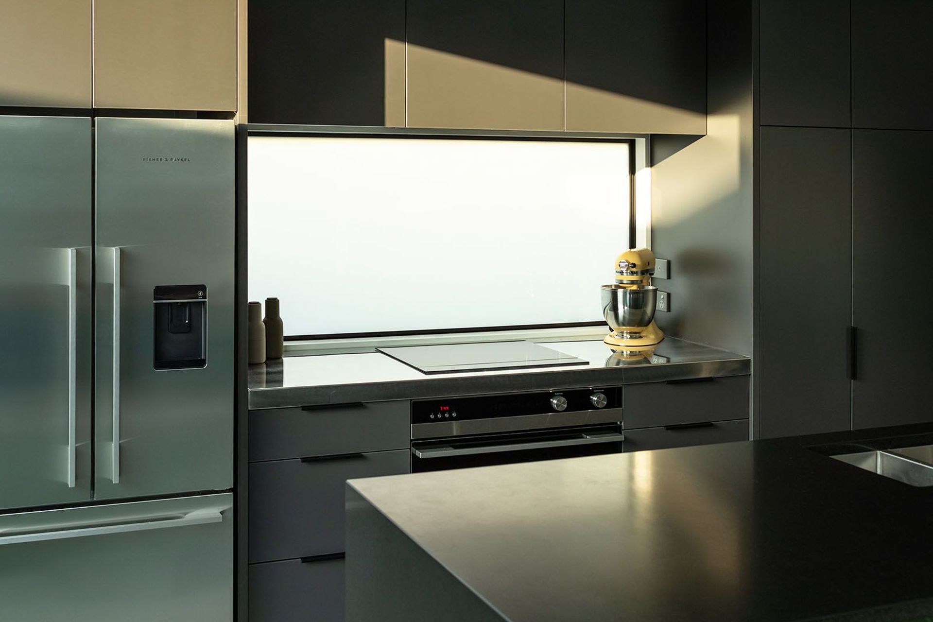 A reflective splashback and stone benchtop are complemented by Fisher & Paykel appliances.