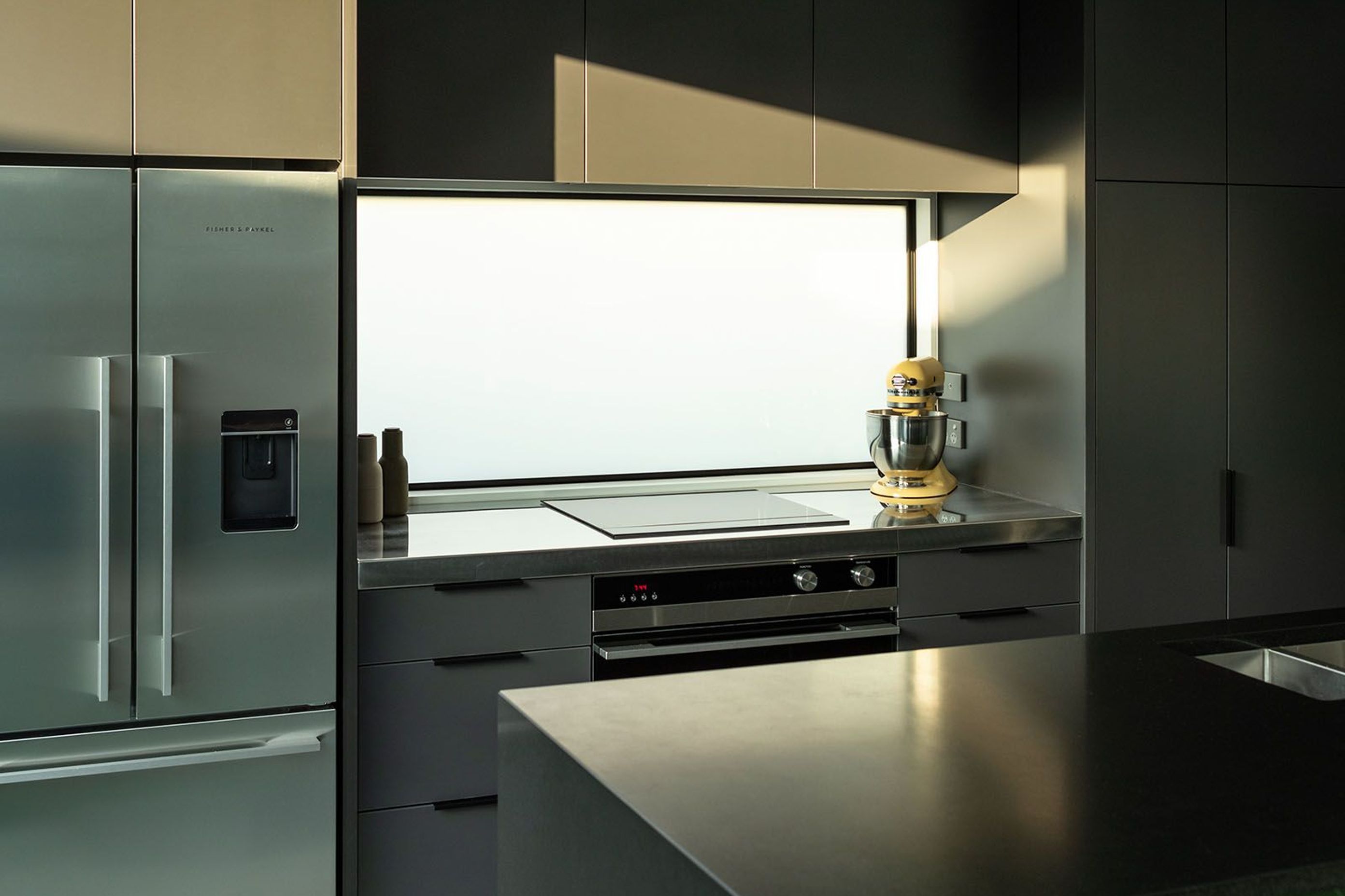 A reflective splashback and stone benchtop are complemented by Fisher &amp; Paykel appliances.
