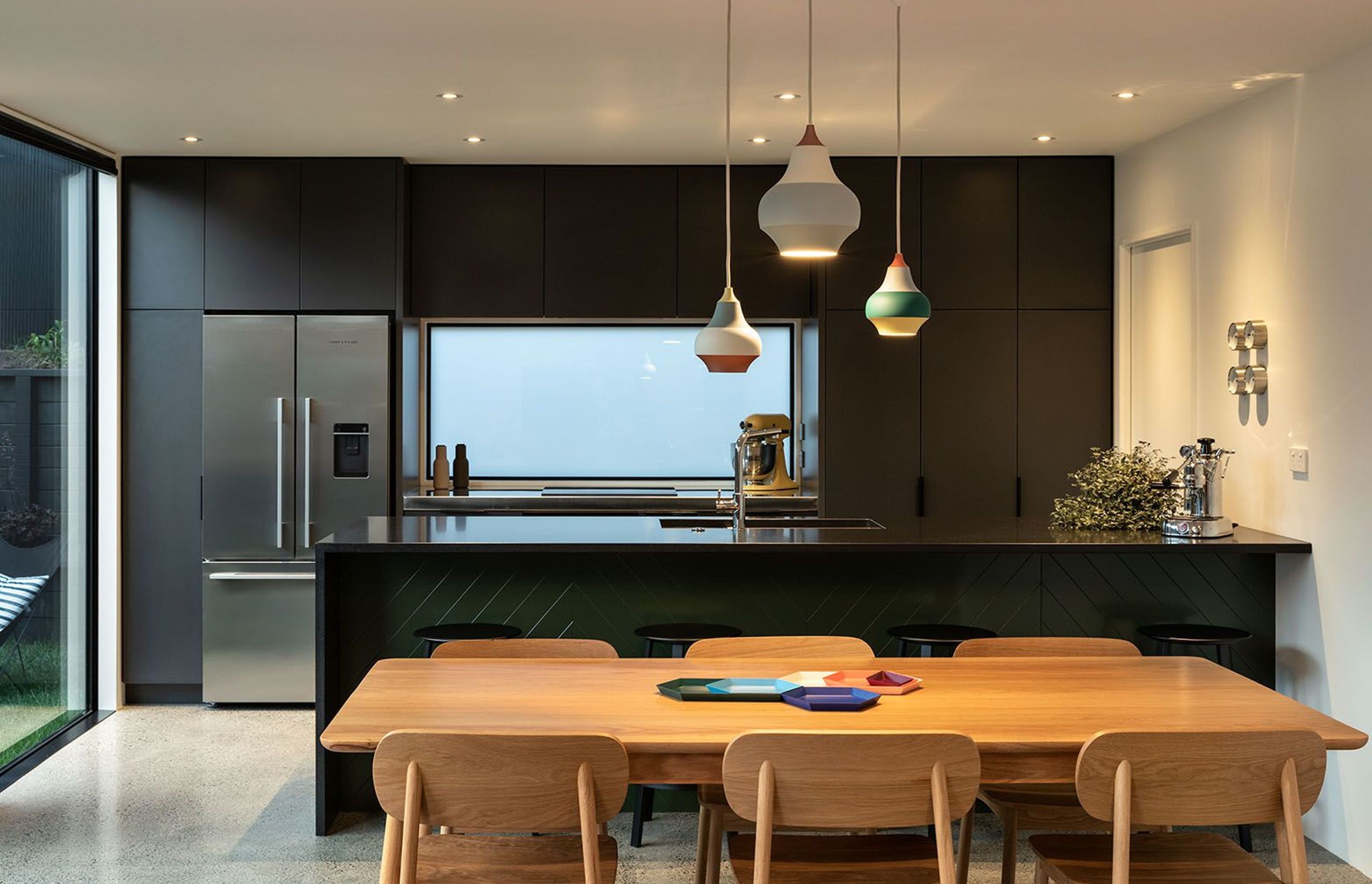 A dark green and grey kitchen draws on Blackbird's dark exterior, providing a contrast to the polished concrete flooring and timber table and chairs.