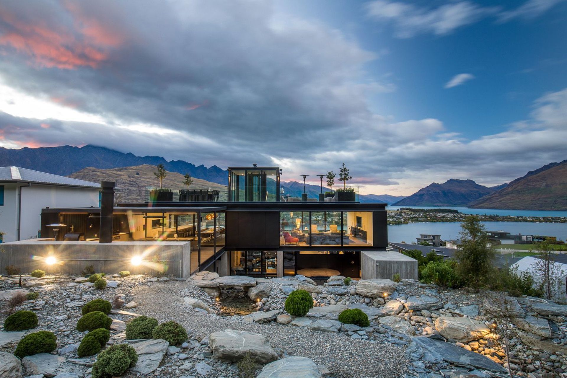 The north-facing elevation of Cascata House seen in context to Lake Wakatipu and the surrounding mountains, viewed from the rockery garden and stream.