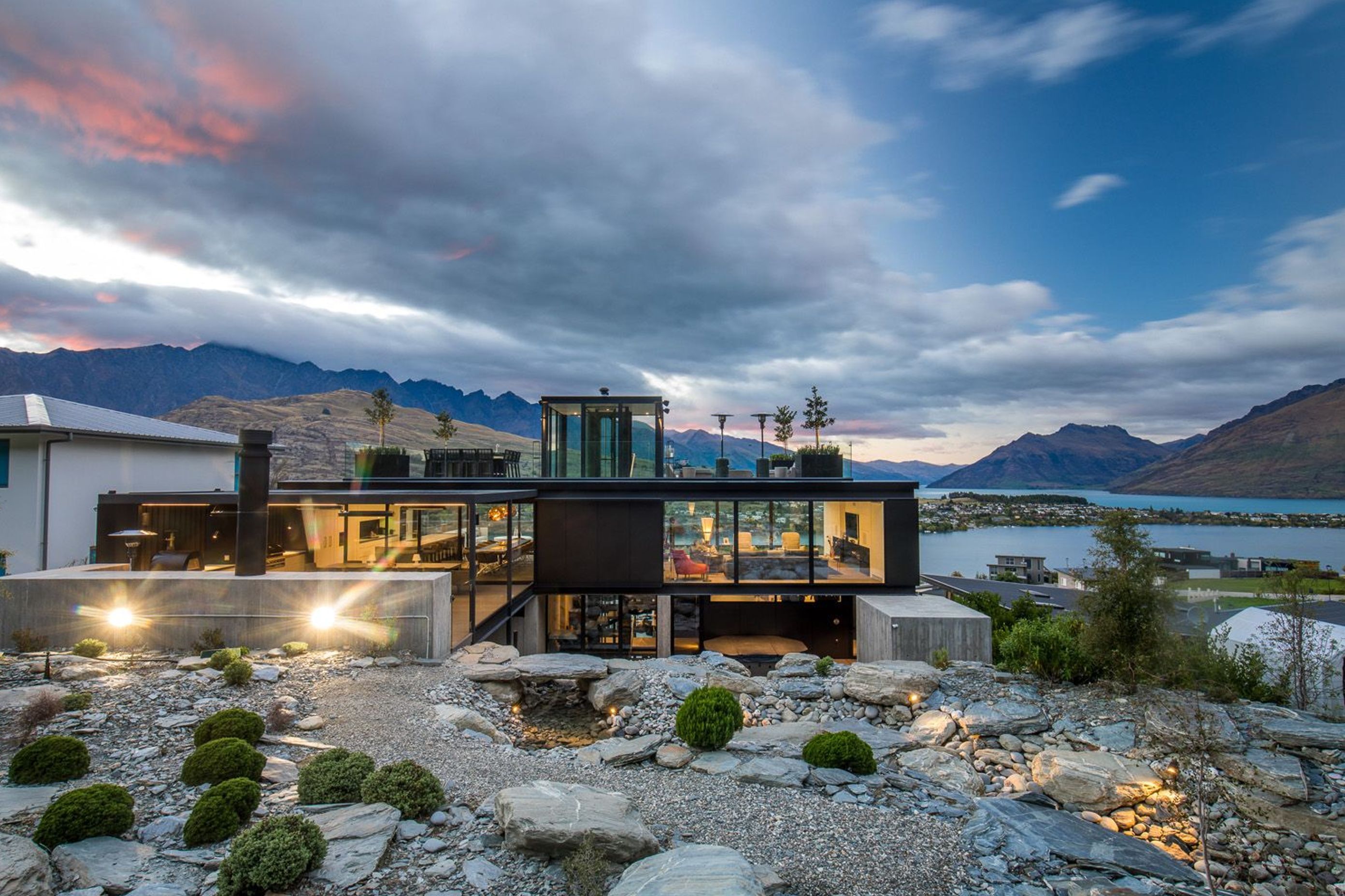 The north-facing elevation of Cascata House seen in context to Lake Wakatipu and the surrounding mountains, viewed from the rockery garden and stream.