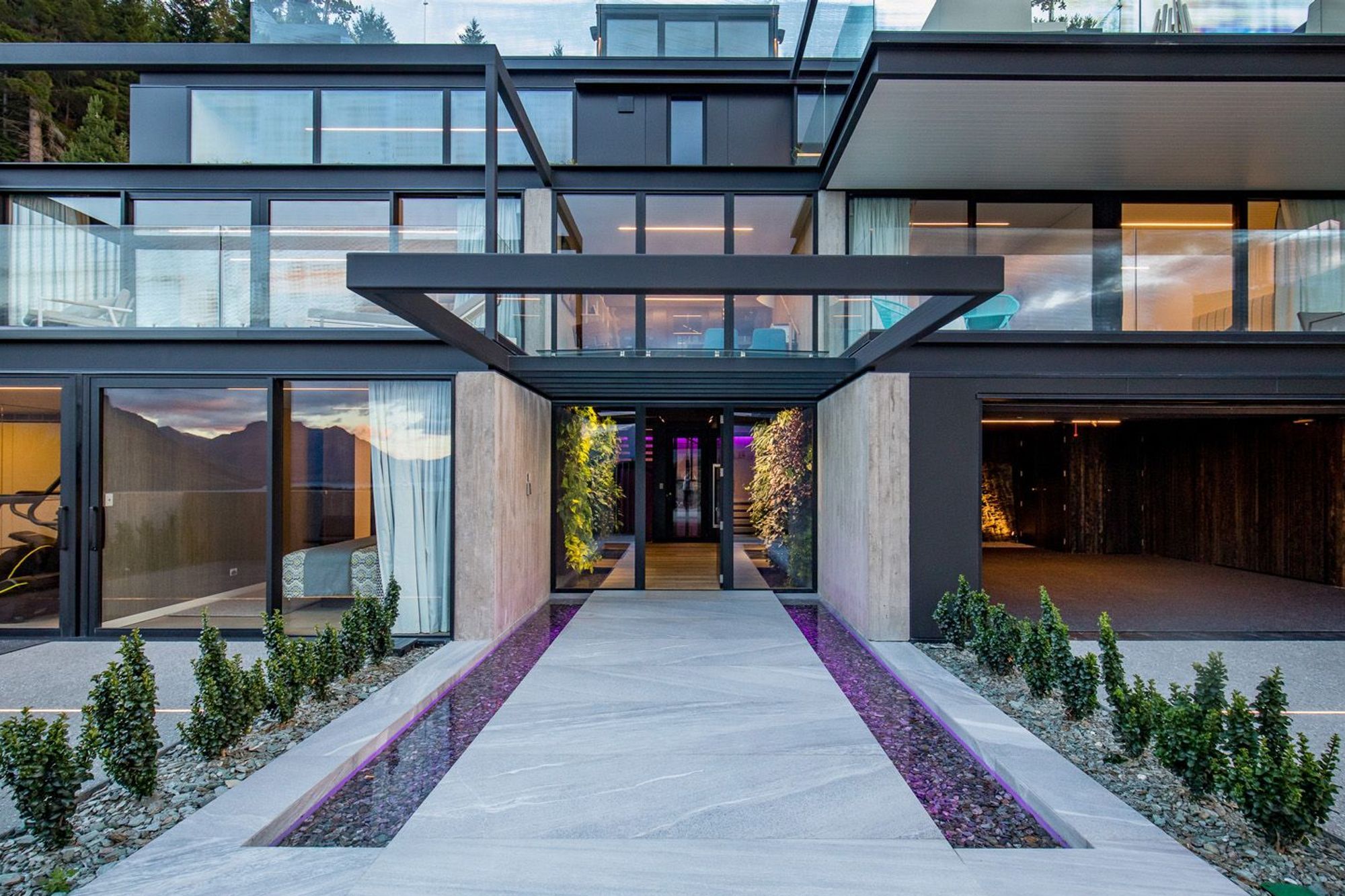 The entry court features stone reflection ponds and vertical green walls, underlit with colour changing LED lighting strips, and covered by a glazed roof on cantilevered steel beams.