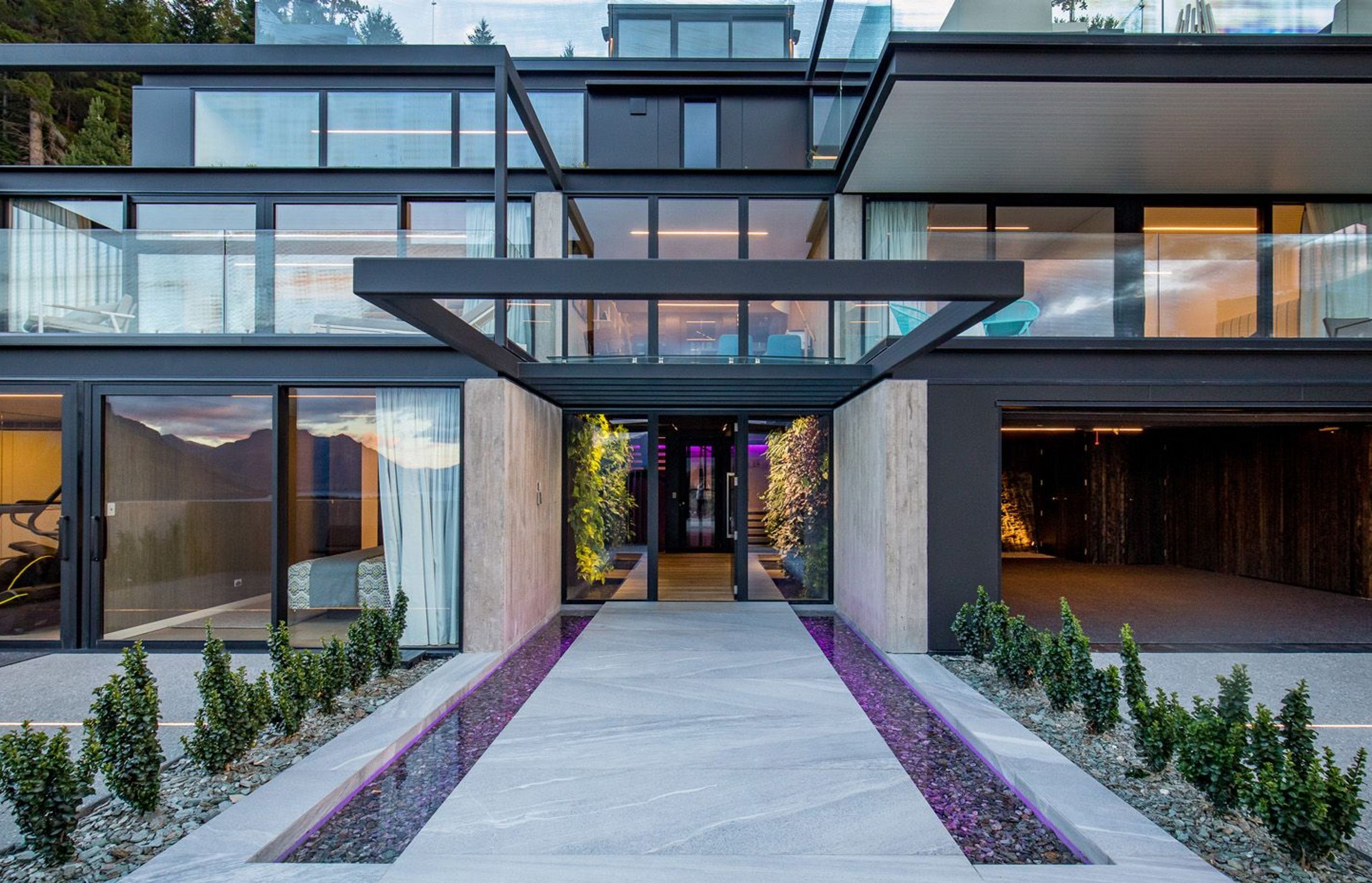 The entry court features stone reflection ponds and vertical green walls, underlit with colour changing LED lighting strips, and covered by a glazed roof on cantilevered steel beams.