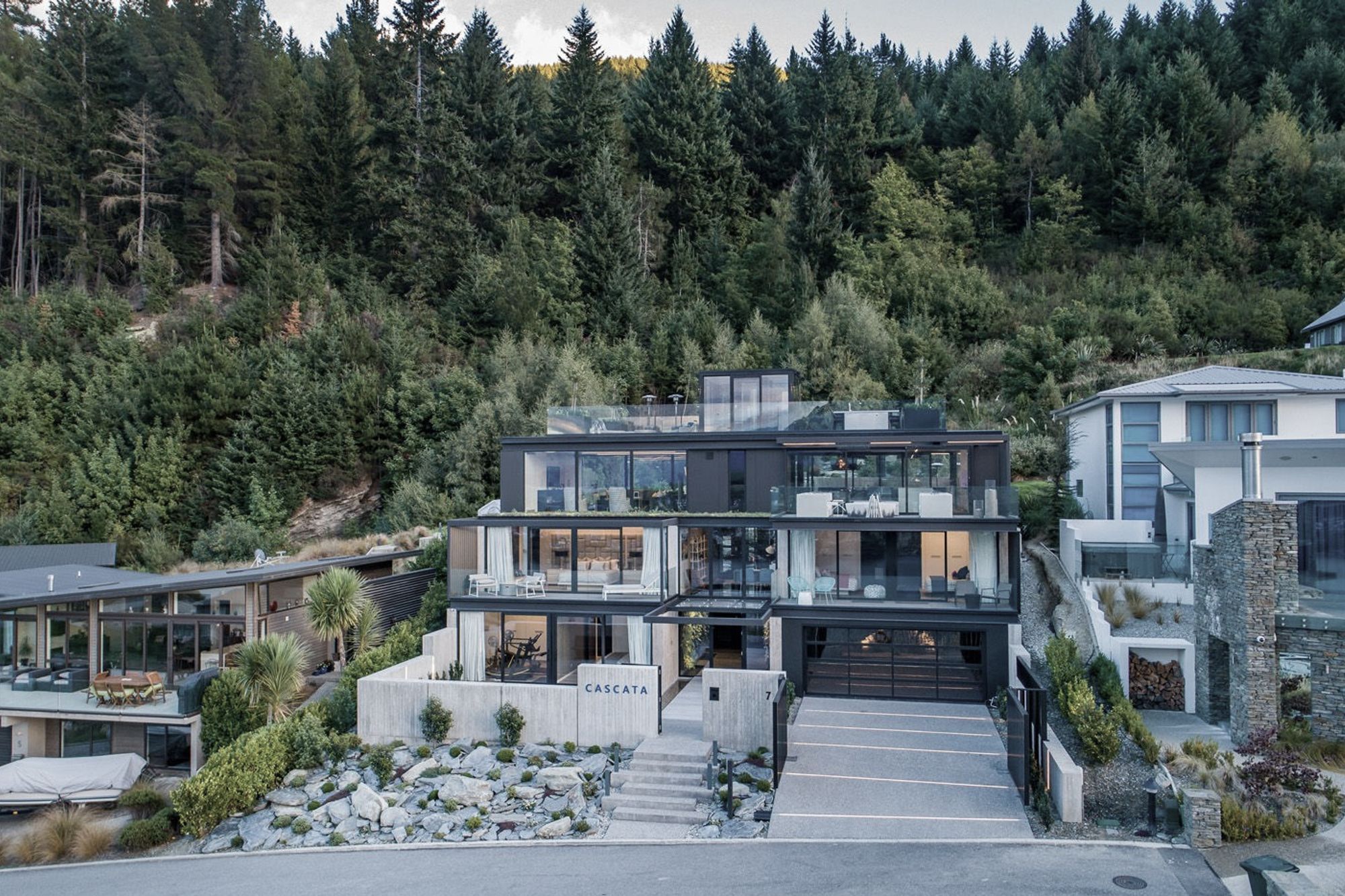The south-facing elevation seen from the lake's edge, with its backdrop of forest reserve, where the house is steeped and terraced into the sloping rock terrain.