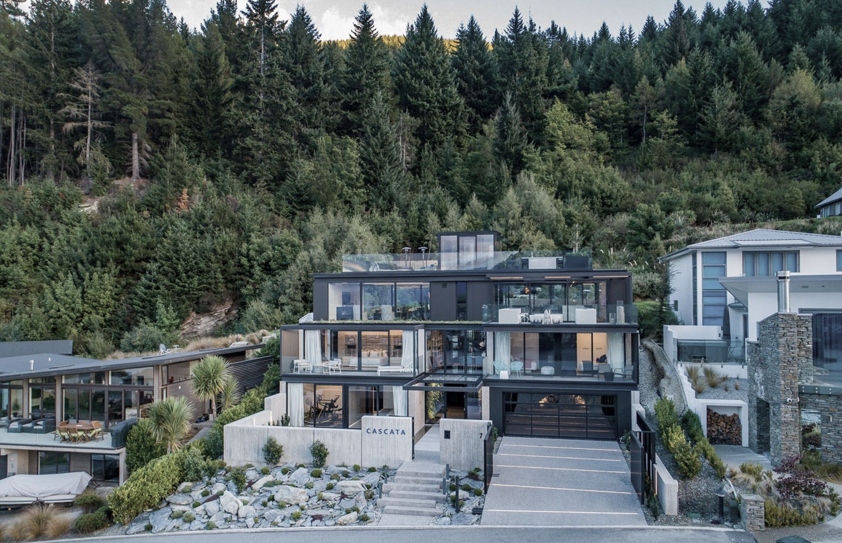 The south-facing elevation seen from the lake's edge, with its backdrop of forest reserve, where the house is steeped and terraced into the sloping rock terrain.