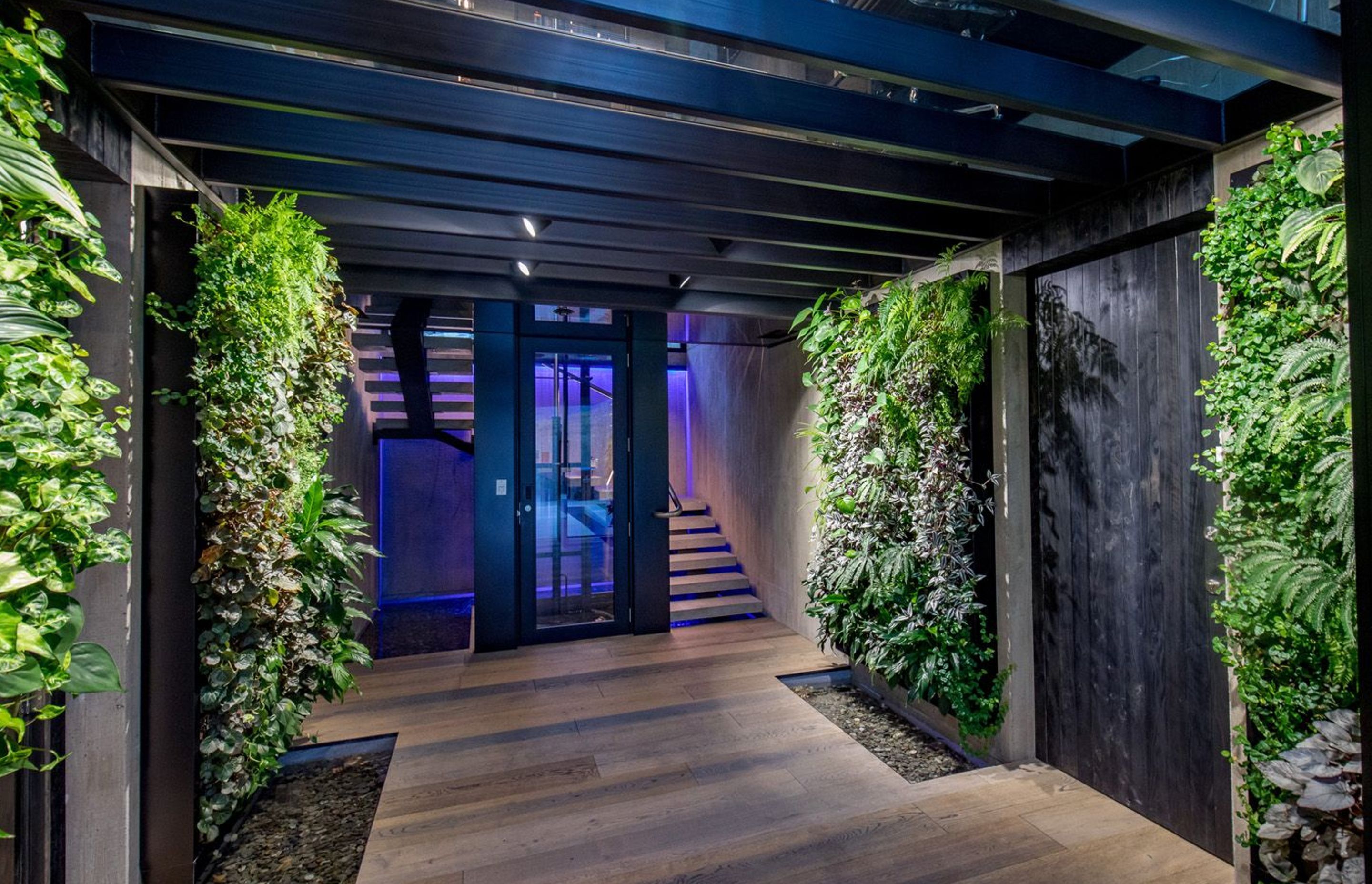 The entrance foyer, lined in vertical green walls, leading to the central lift shaft and stairwell, with a glass ceiling above, and an internal waterfall on the rear stairwell wall beyond.