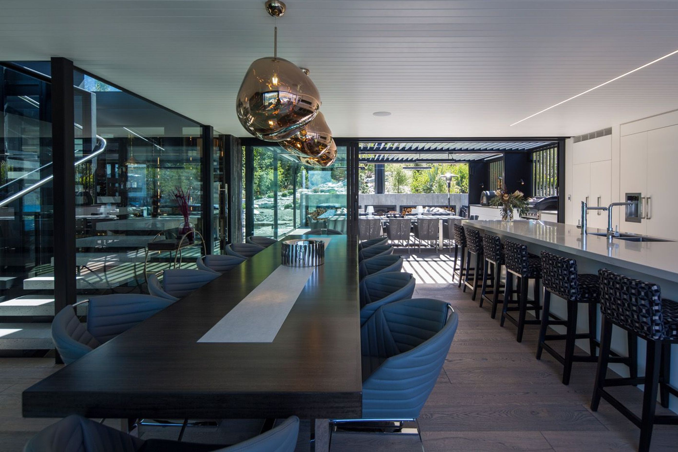 Looking from the dining area across the kitchen to the sheltered outdoor room, the rockery garden and the forest beyond. The bar and stairwell are adjacent.