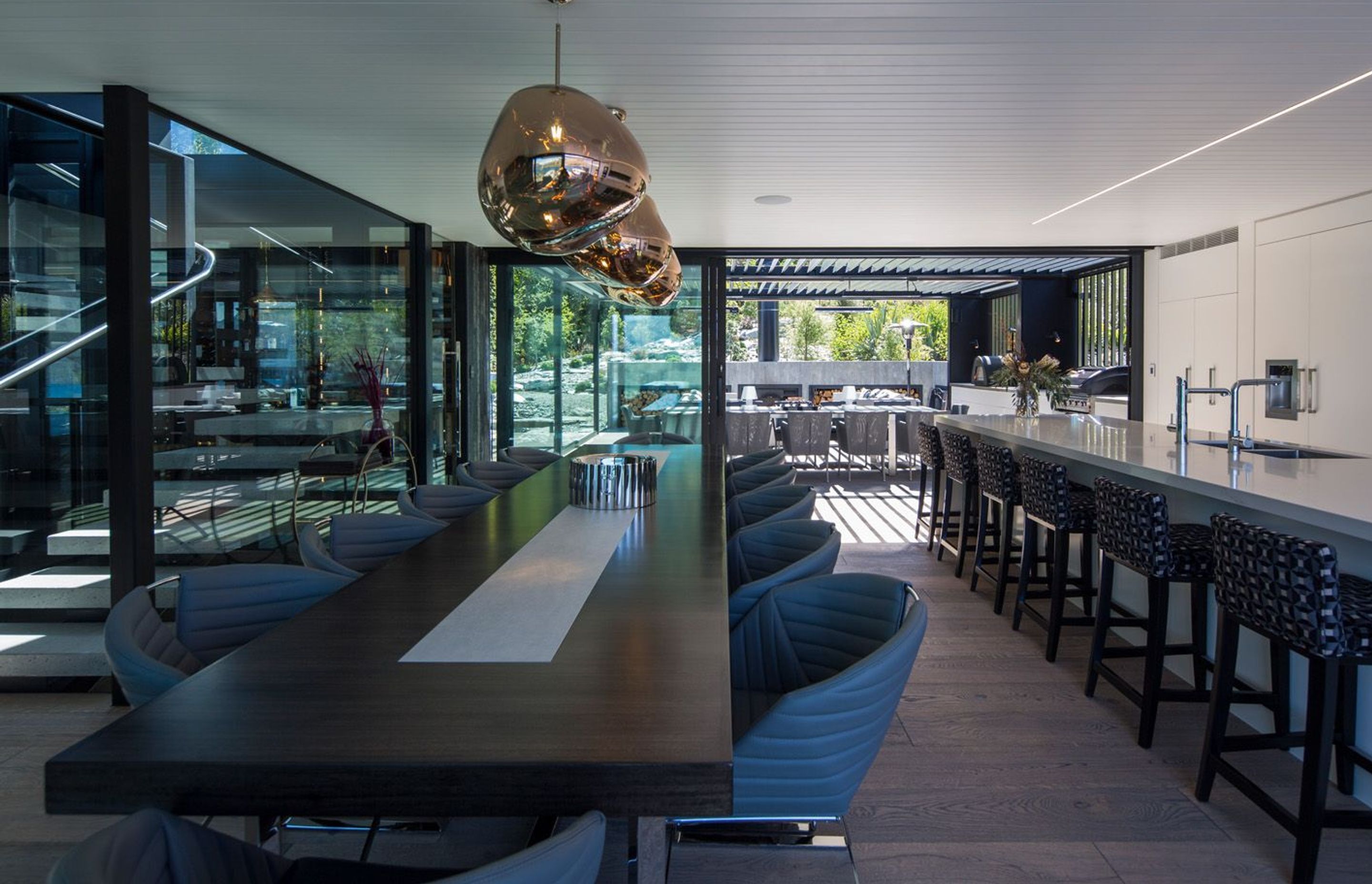 Looking from the dining area across the kitchen to the sheltered outdoor room, the rockery garden and the forest beyond. The bar and stairwell are adjacent.