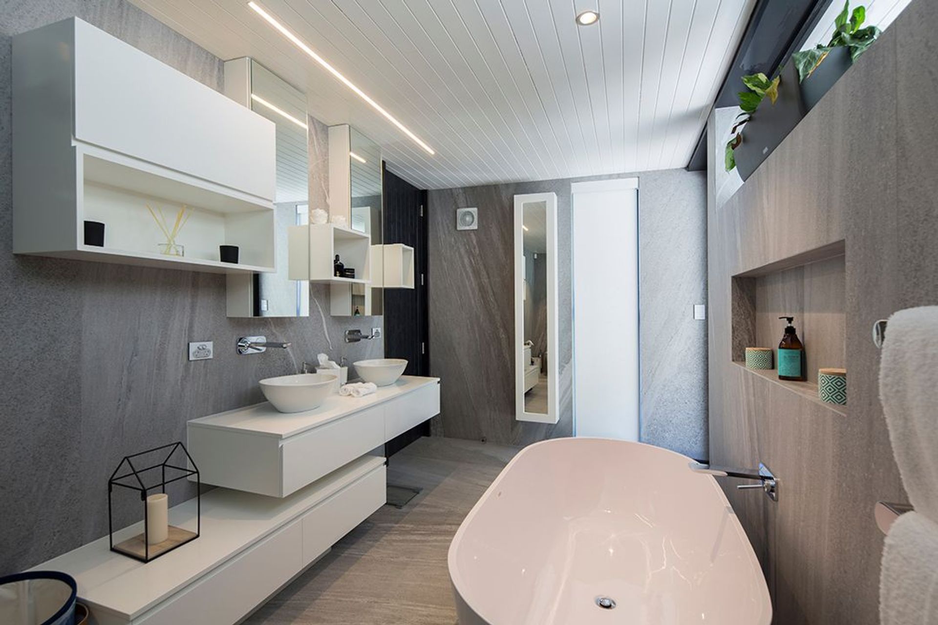The ensuite bathroom is crisp and clean in grey stone and white. White stone bath, basins, joinery and ceilings reflect a minimalist colour palette.