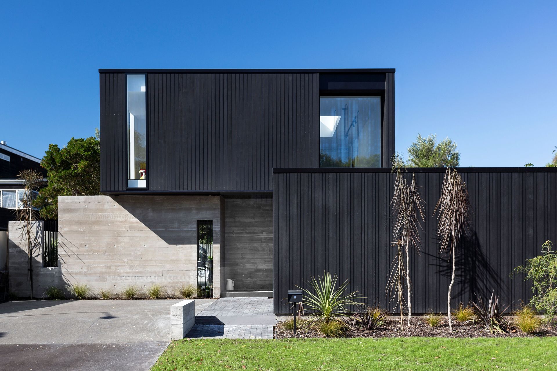 Churchill is comprised of a black cedar-clad box lightly resting over two in-situ concrete walls, with another black box out front forming the garage and boundary fence.