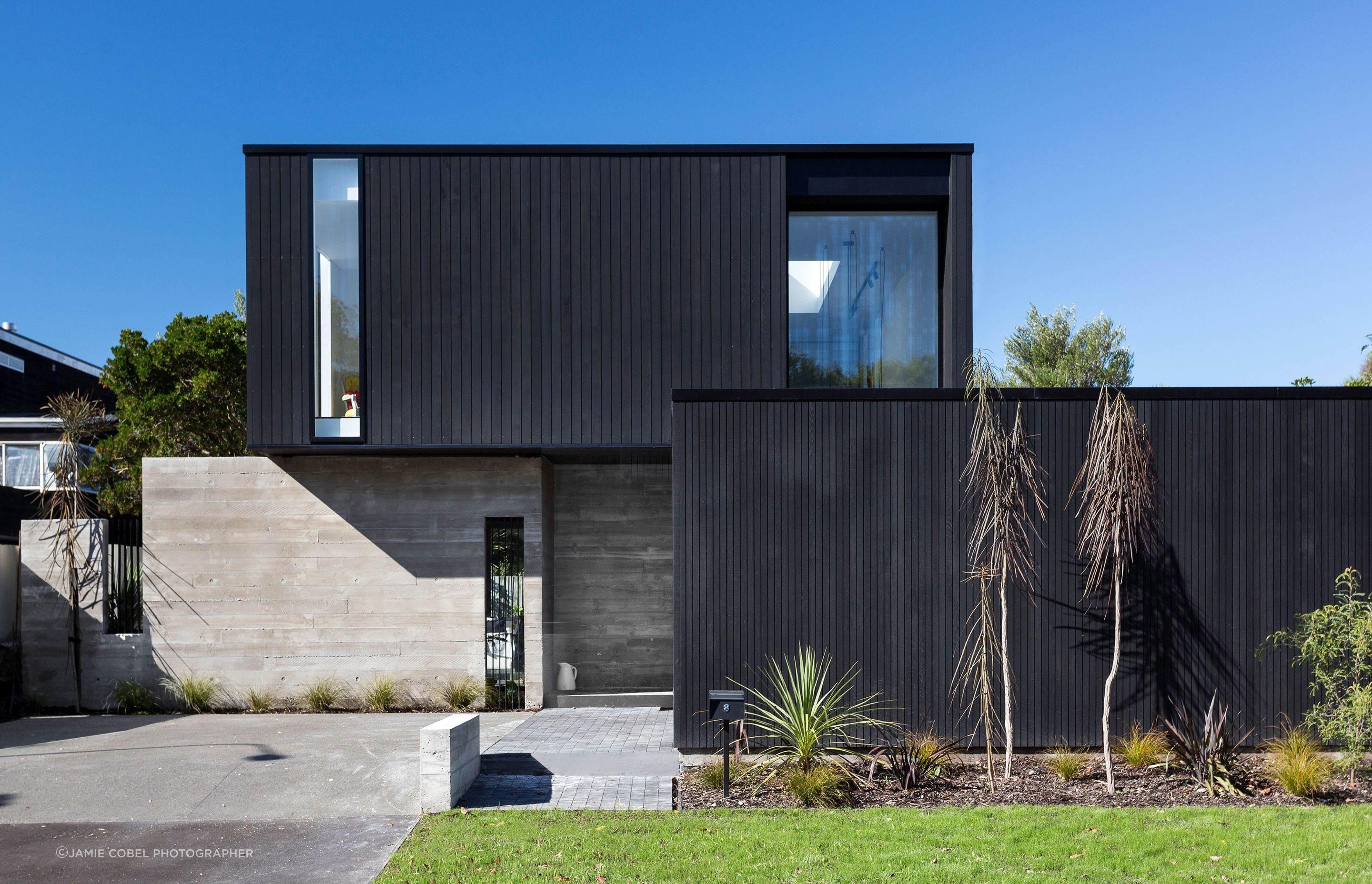 Churchill is comprised of a black cedar-clad box lightly resting over two in-situ concrete walls, with another black box out front forming the garage and boundary fence.