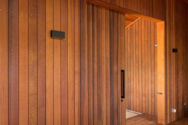 Warm, richly toned timber-lined interior featuring vertical wood wall panelling, a matching timber doorway and door, and a small glimpse of timber flooring beyond. The image emphasizes the continuous built-in wood finish and clean linear detailing.