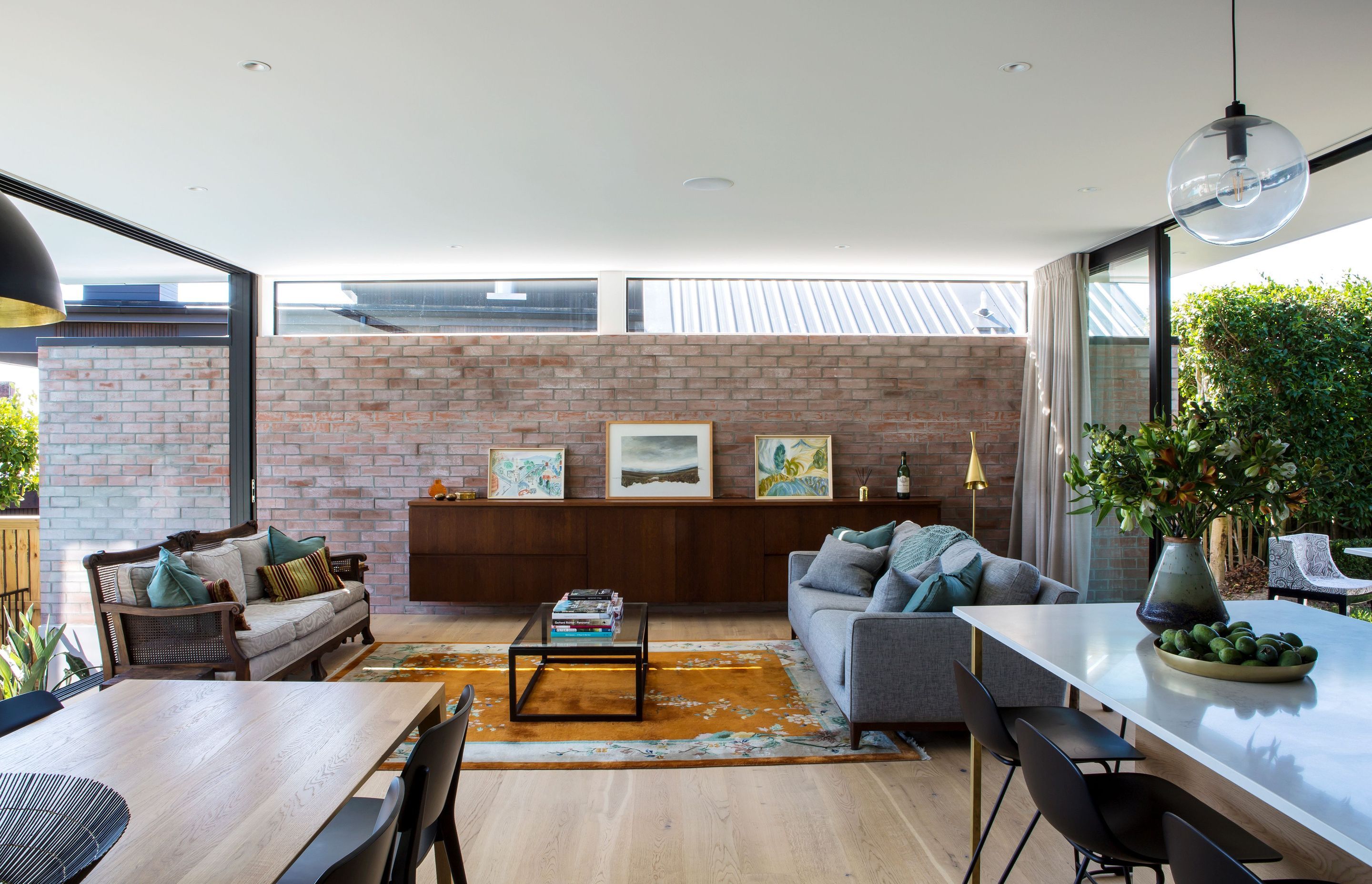 The open-plan lounge and dining area opens up on both sides to patio areas, with clerestory windows above a feature brick wall drawing light into the space.