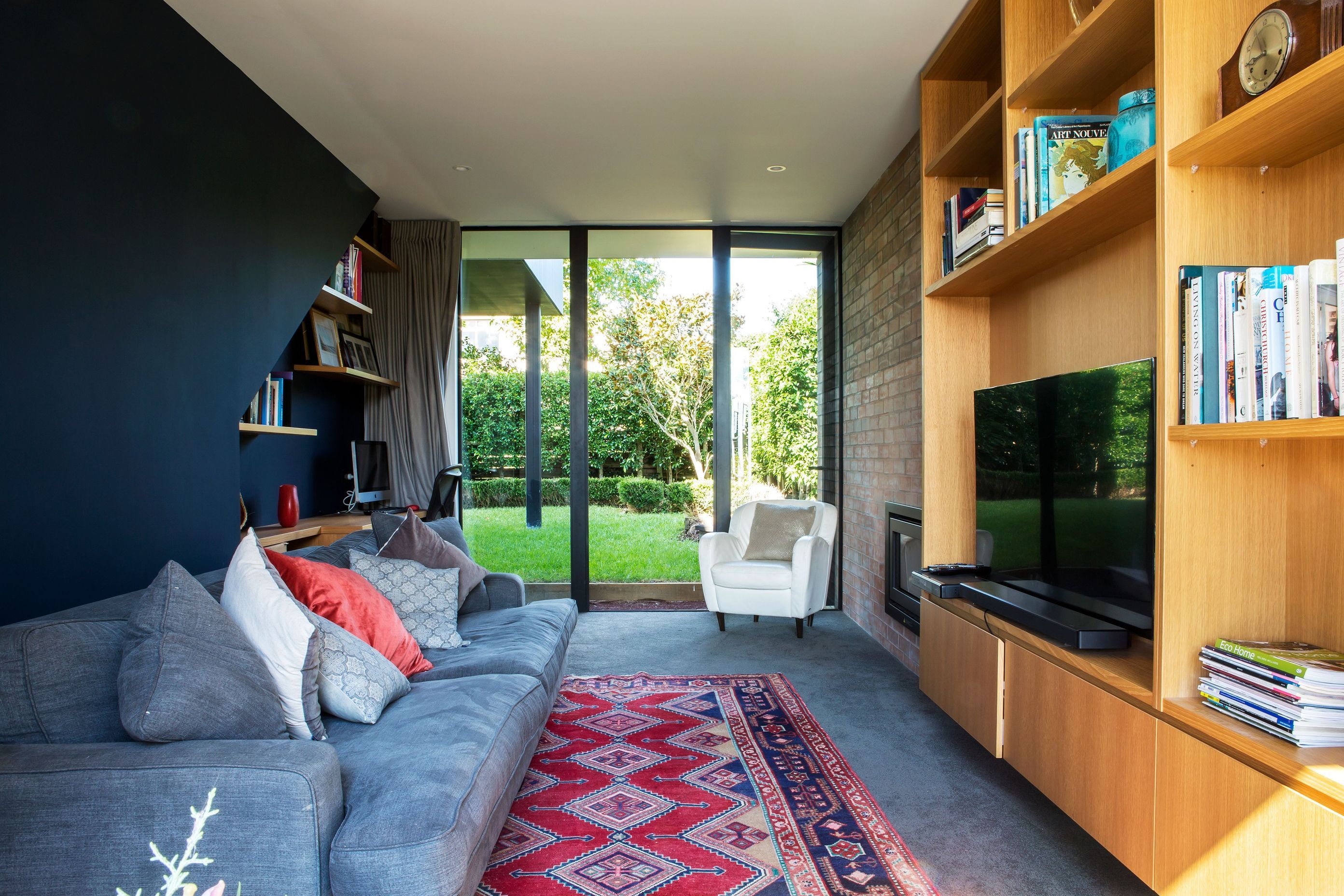 The cosy media room features a brick wall with a fireplace and bespoke timber cabinetry for the television on one side of the room and a built-in office space on the opposite wall.