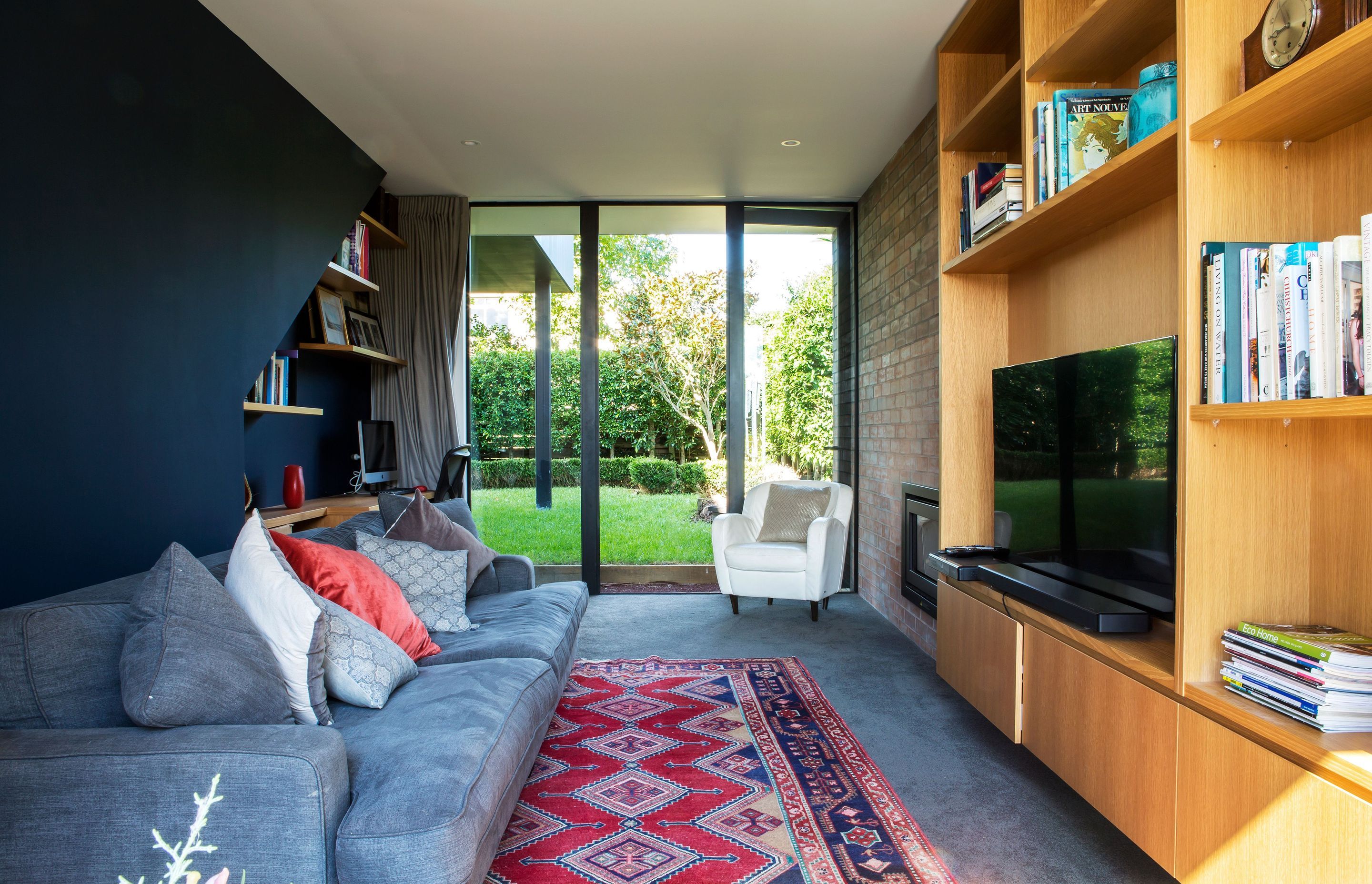 The cosy media room features a brick wall with a fireplace and bespoke timber cabinetry for the television on one side of the room and a built-in office space on the opposite wall.