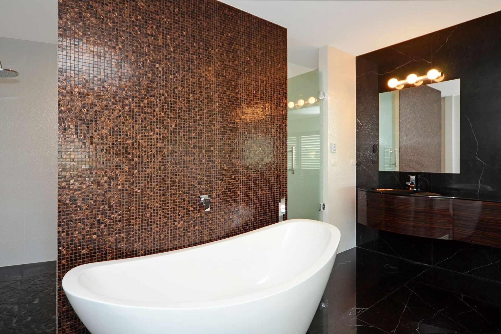 A free standing bath is backs by glass mosaics.