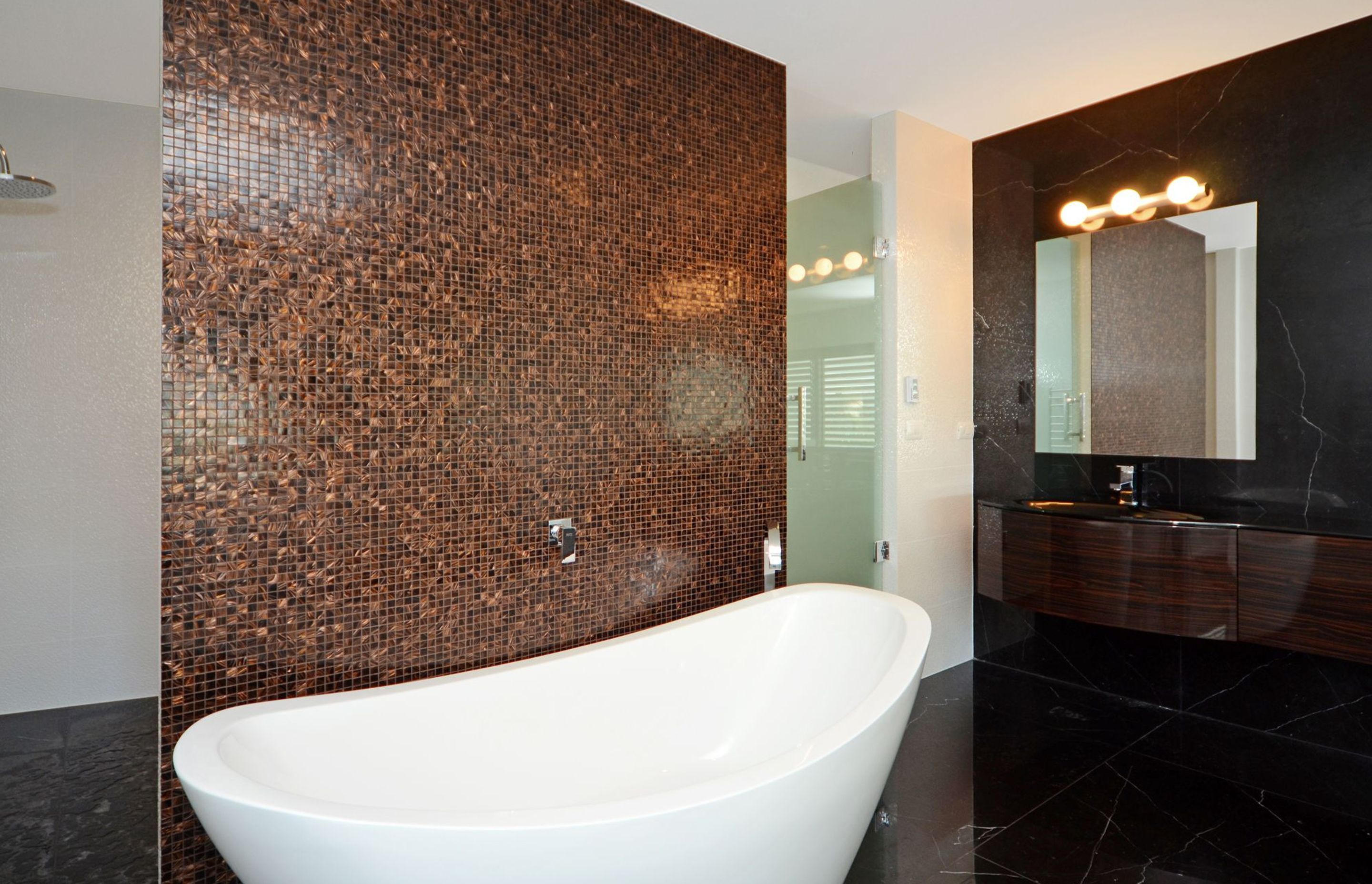 A free standing bath is backs by glass mosaics.