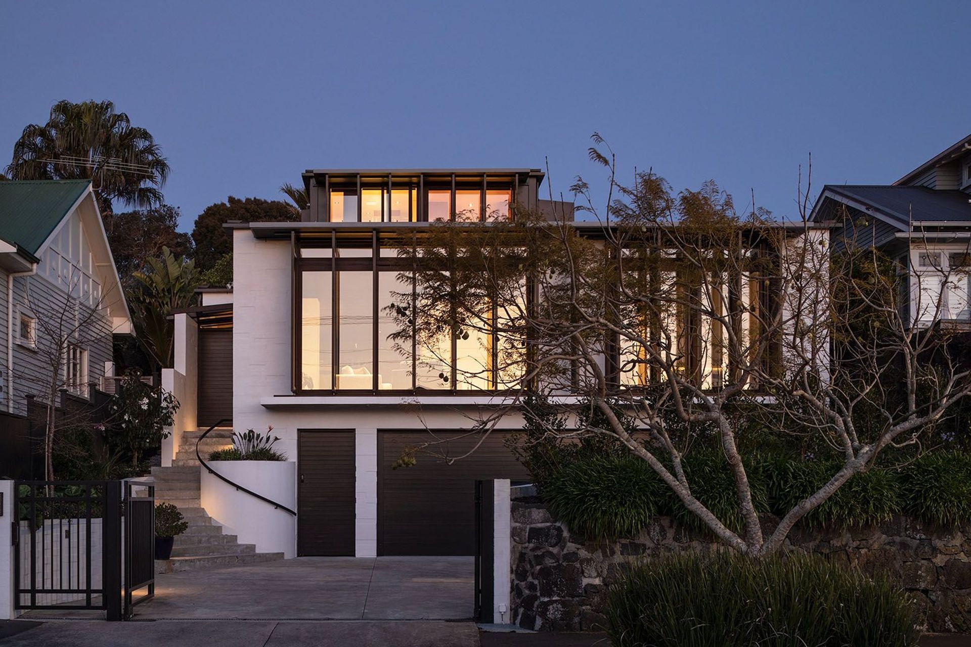 From the street, the western elevation rises across three clear levels—bagged concrete blocks are punctuated with floor-to-ceiling glazing on both the second and third storeys